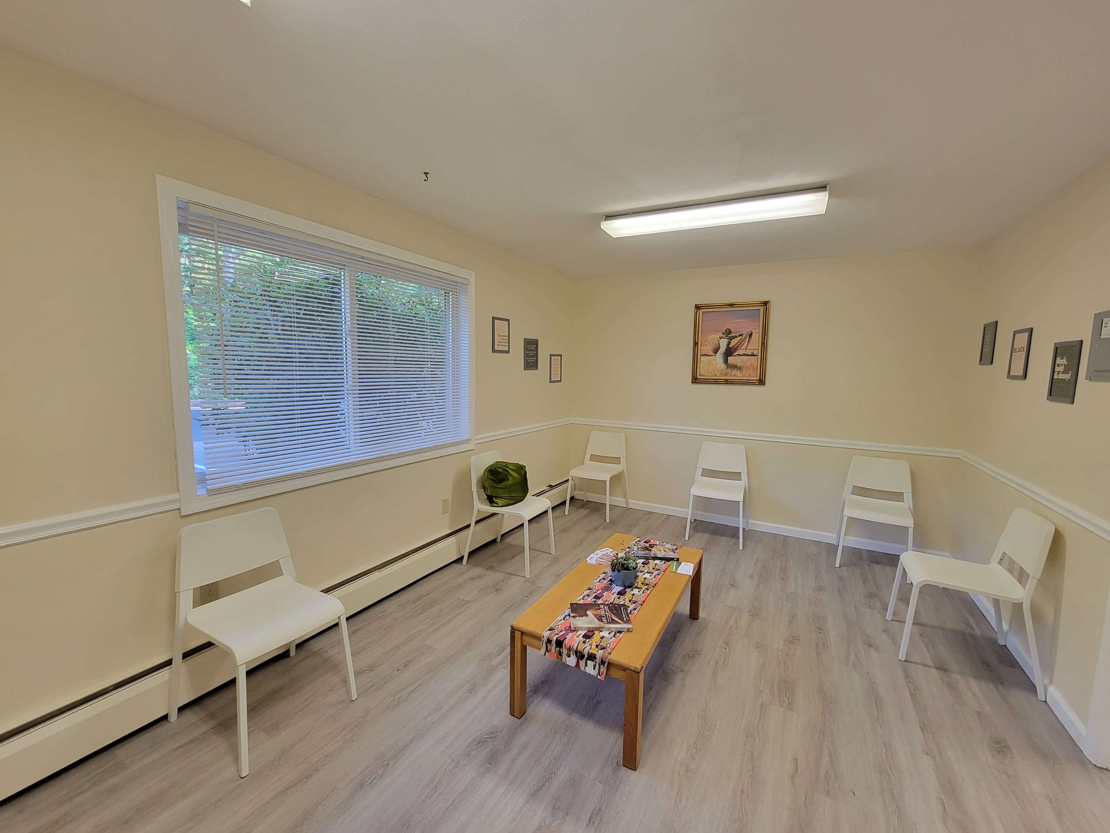 A minimalistic room with light-colored walls, a wooden table in the center, and several white chairs arranged around it.