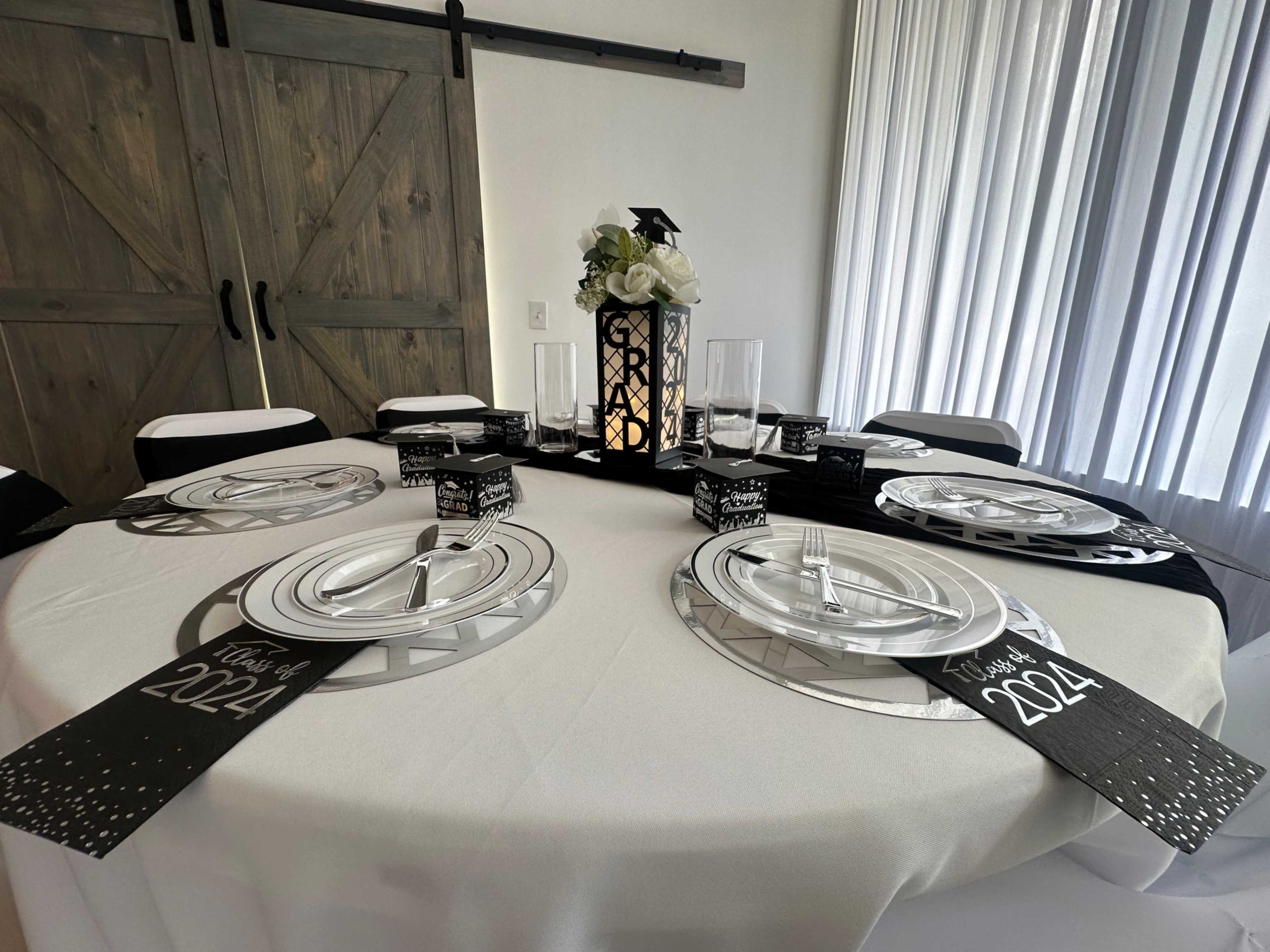 A table set for a graduation celebration features white tablecloths, silver plates, and decorative centerpieces.