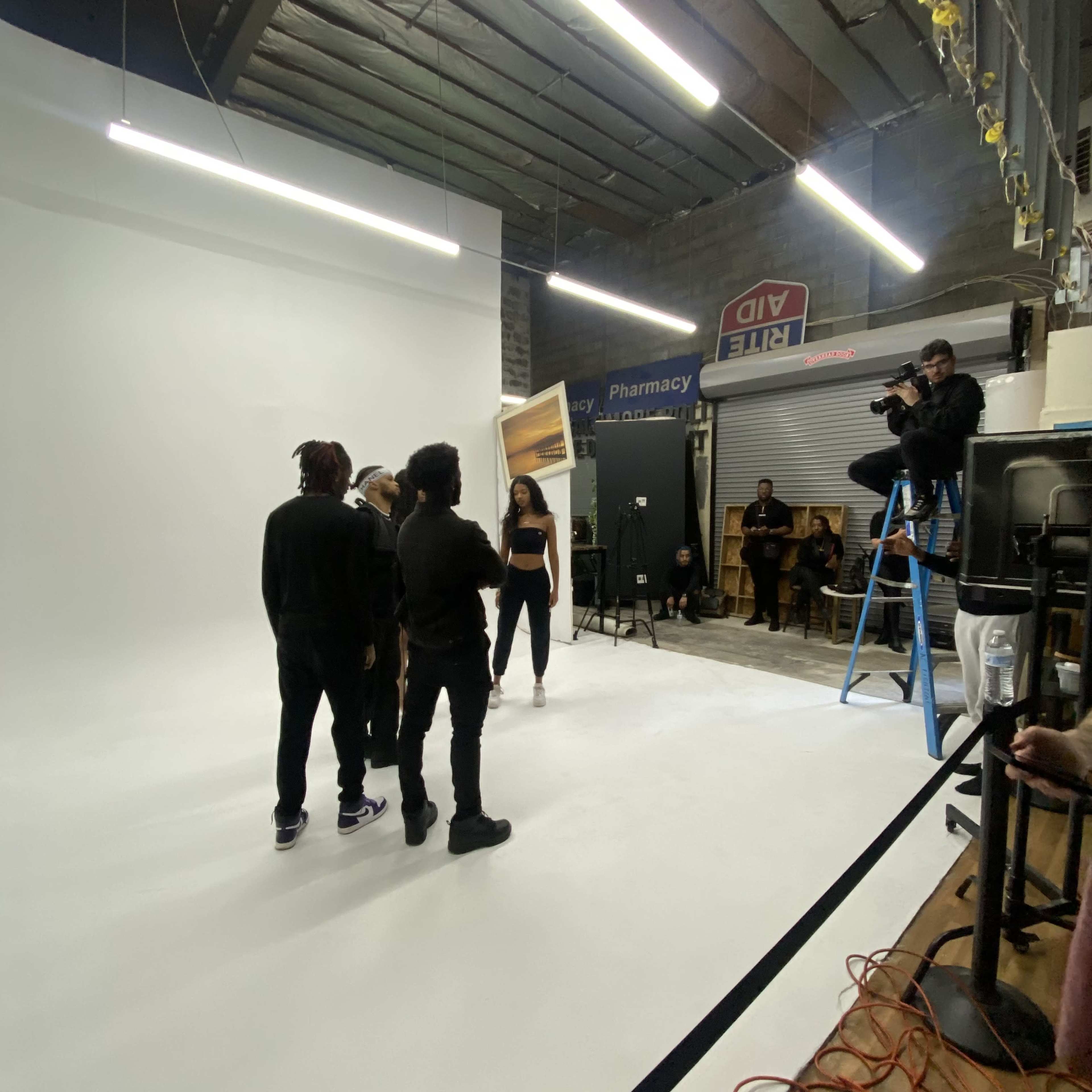 A group of people is gathered in a photography studio, while a person on a ladder adjusts a light fixture.