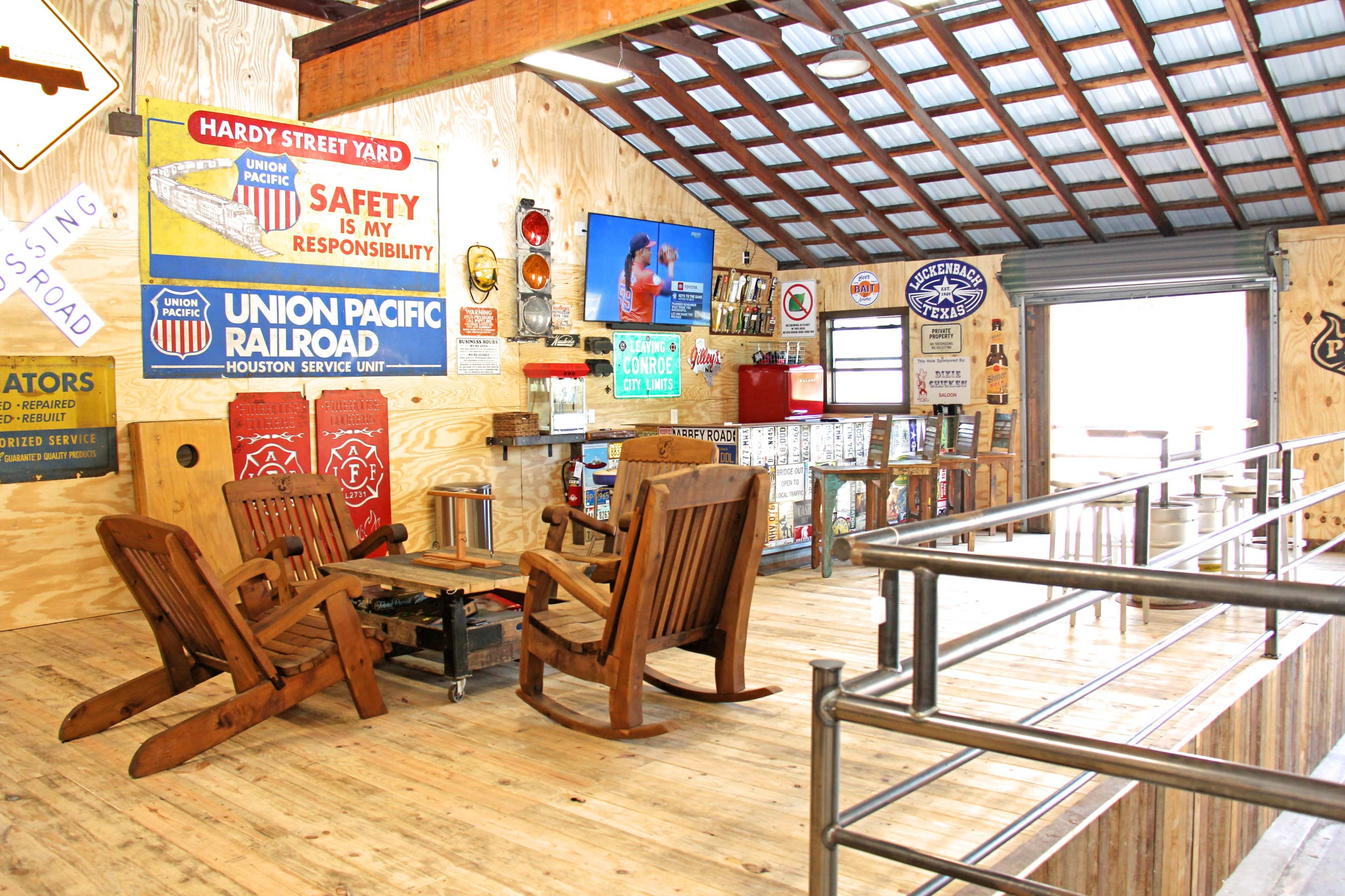A rustic interior with wooden rocking chairs and a coffee table, adorned with vintage railroad and safety signs on the walls.