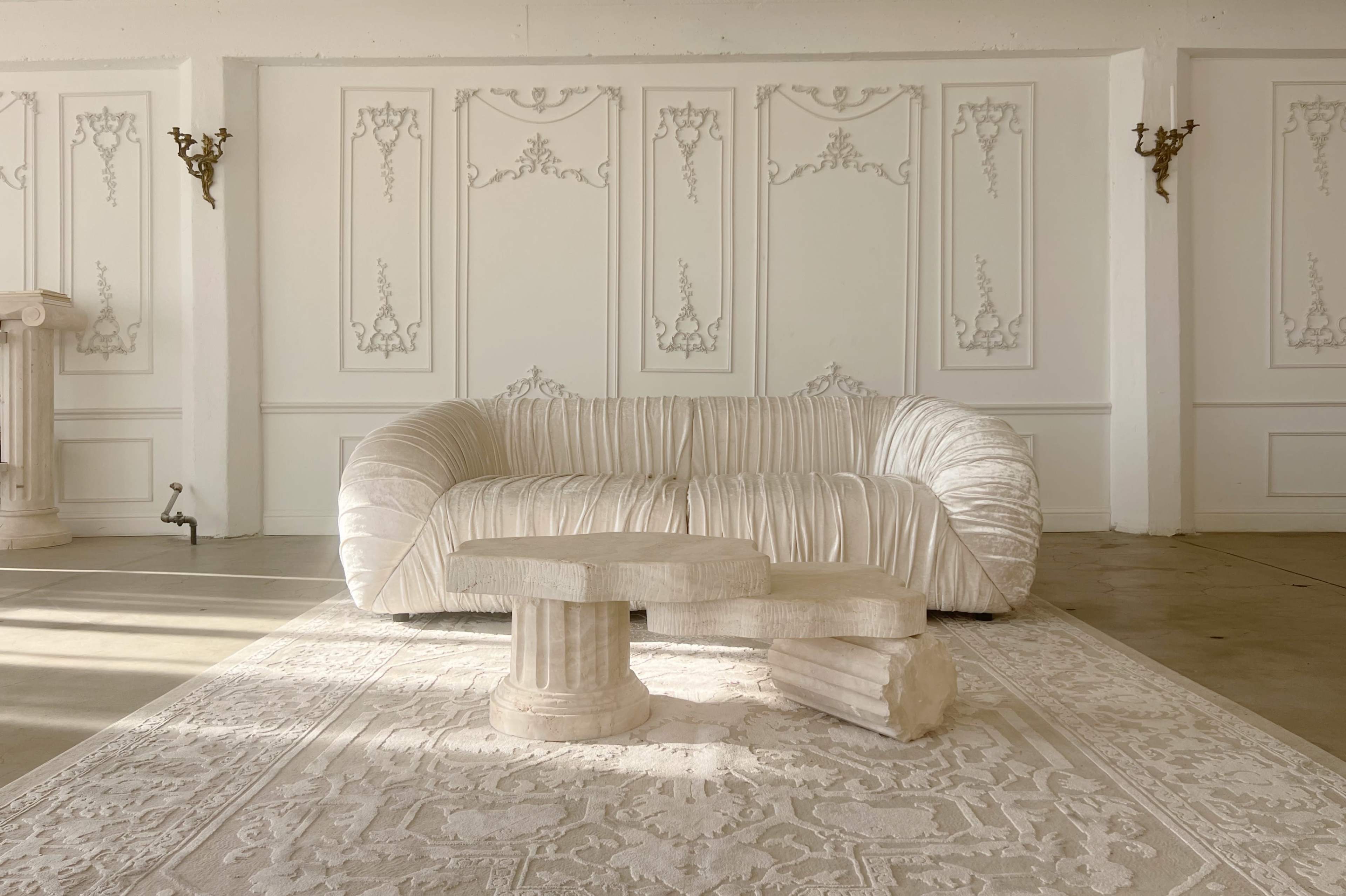 A textured white sofa is positioned in a minimalist room with decorative wall designs and stone furniture.