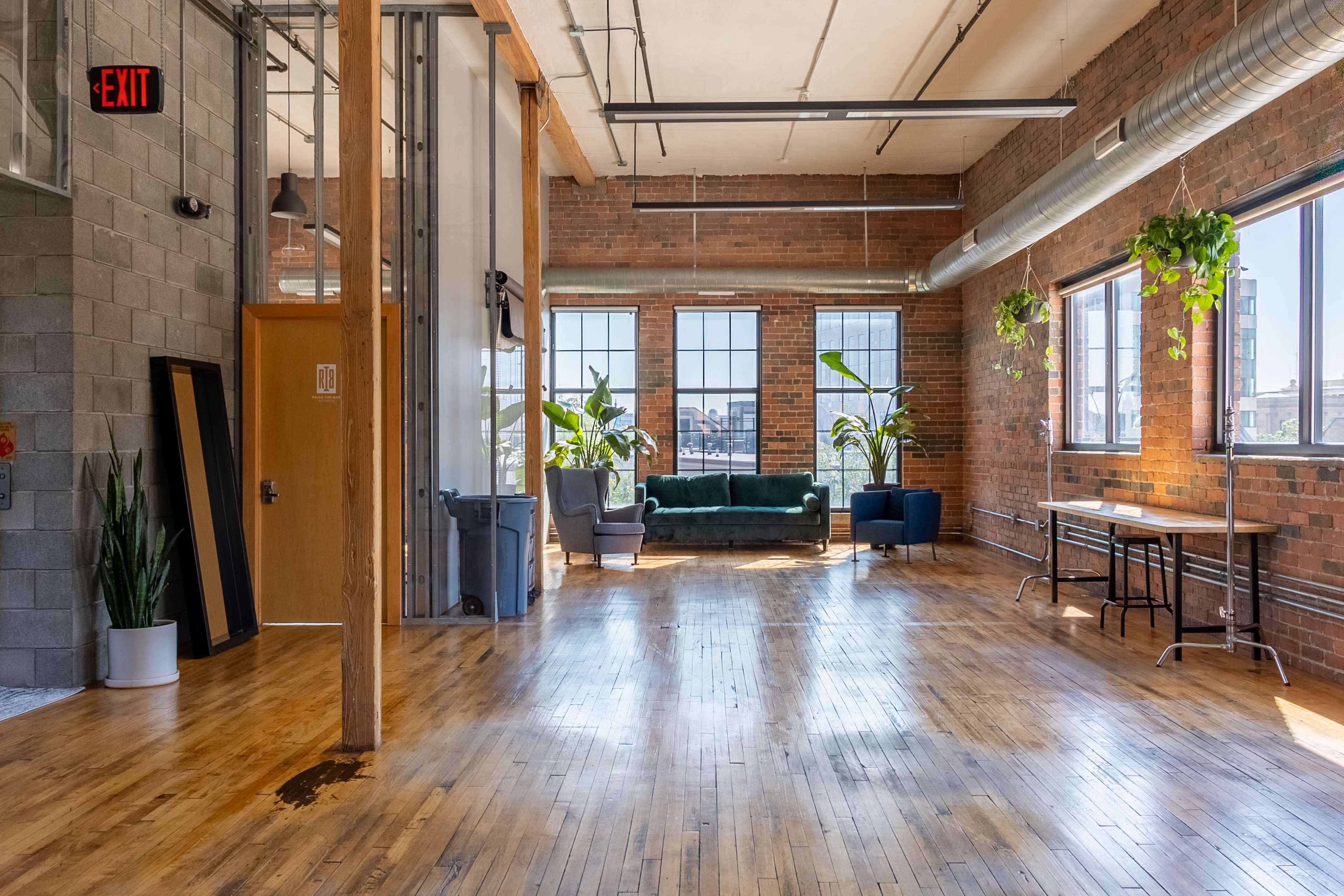 A spacious, open room with large windows, hardwood floors, and a green couch along with plants and a dining table.