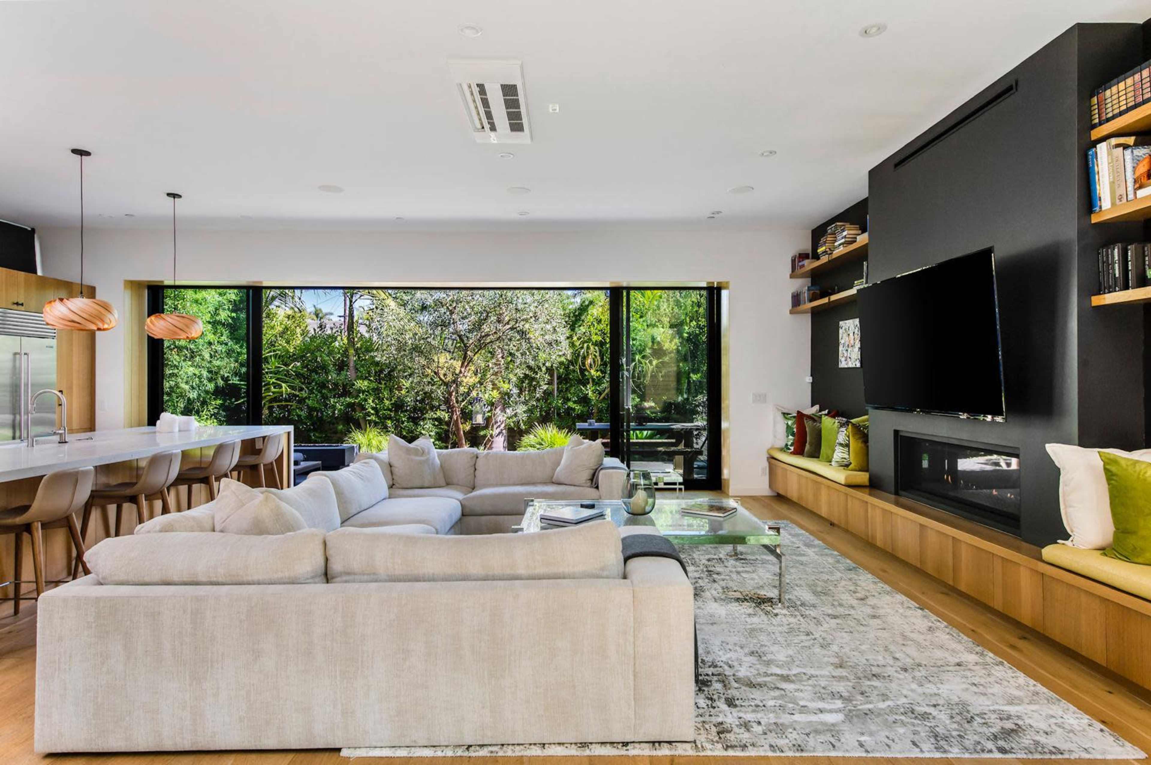 A spacious living room features a large sectional sofa, a glass coffee table, and floor-to-ceiling windows that overlook a garden.