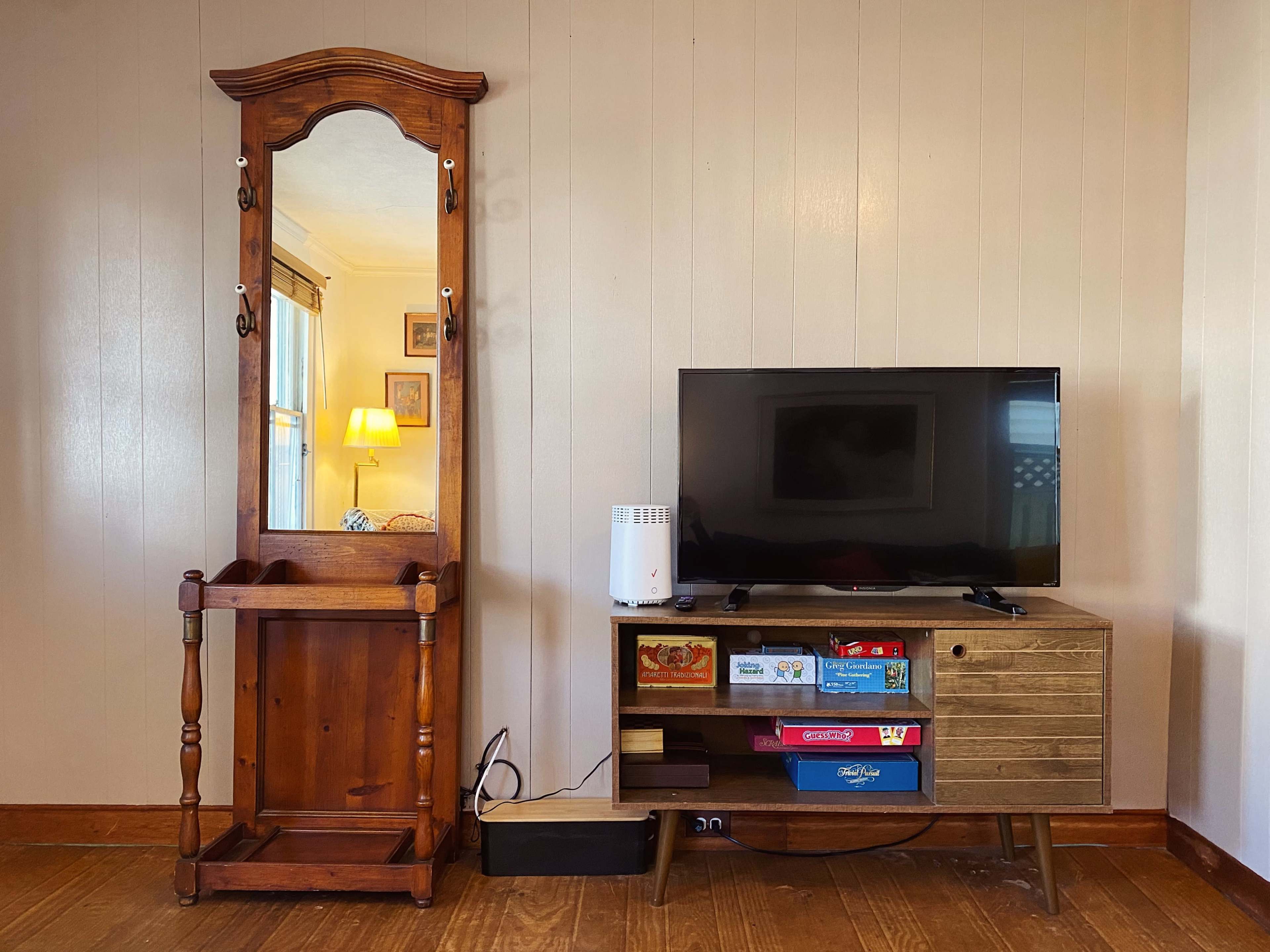 A vintage wooden mirror stand is positioned next to a modern television set on a wooden media console displaying various board games.
