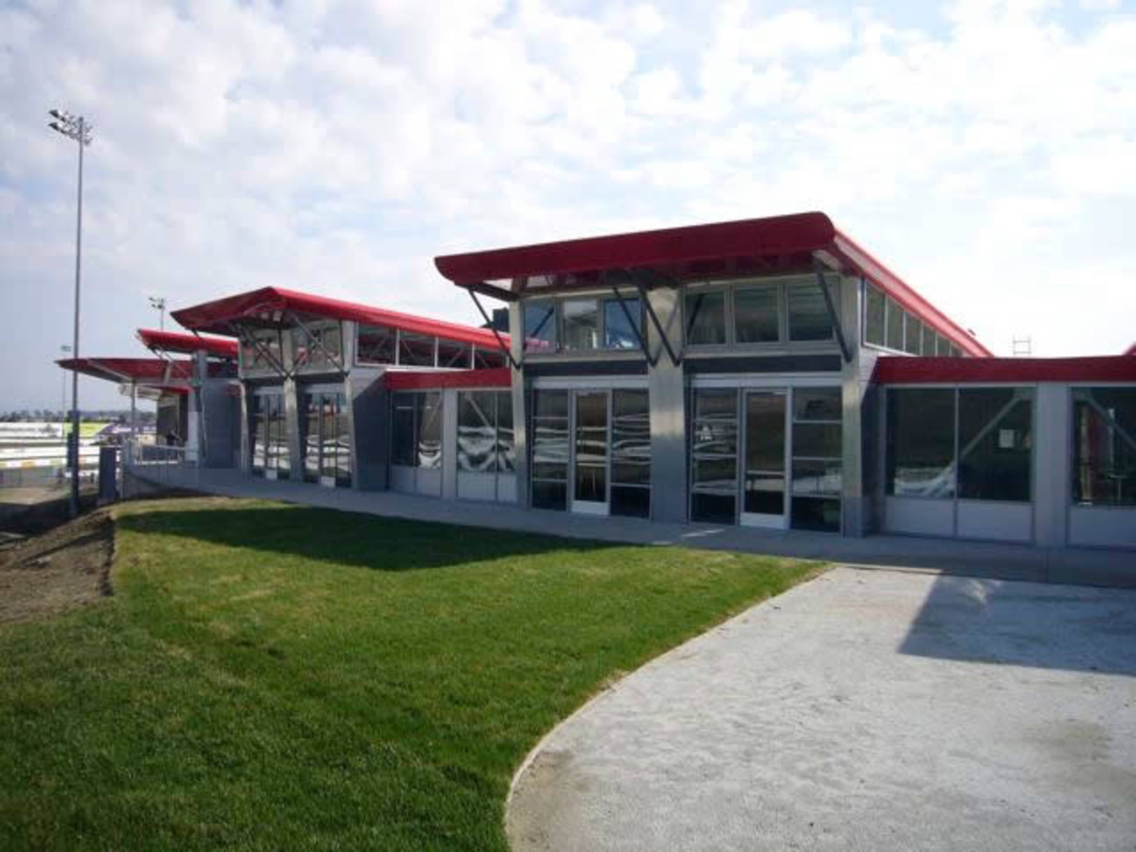 A modern building with a red roof and large glass windows, situated near a grassy area and a paved path.