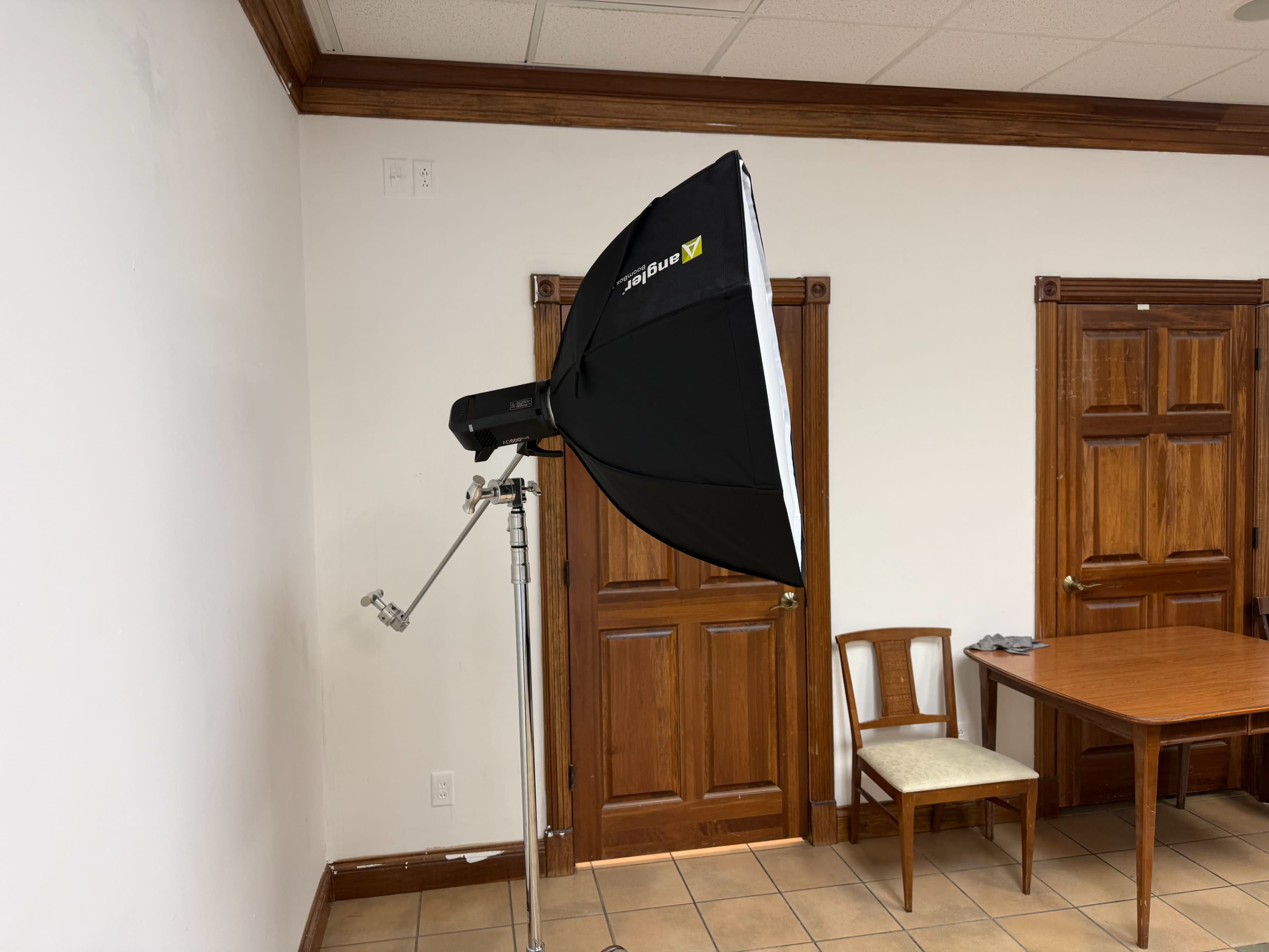 A photography lighting setup is positioned in a room featuring wooden doors and a table with a chair.