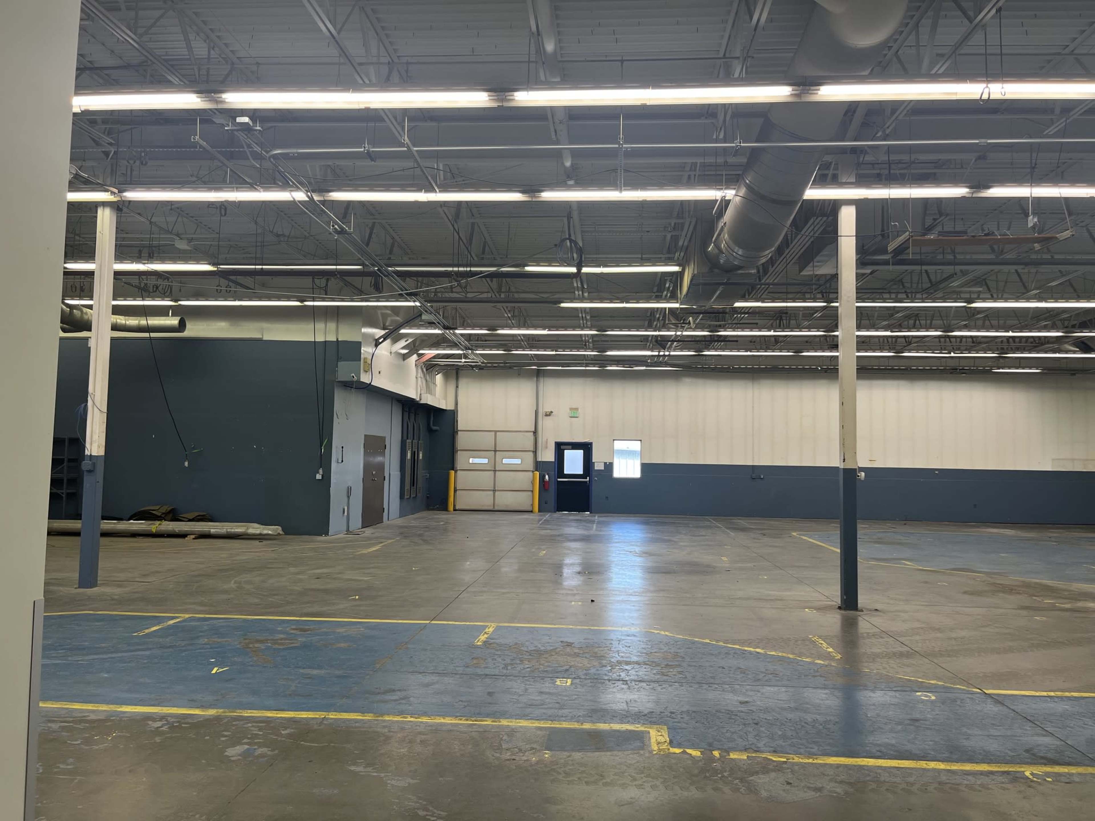 The image shows an empty industrial space with concrete floors, high ceilings, and a loading dock area.