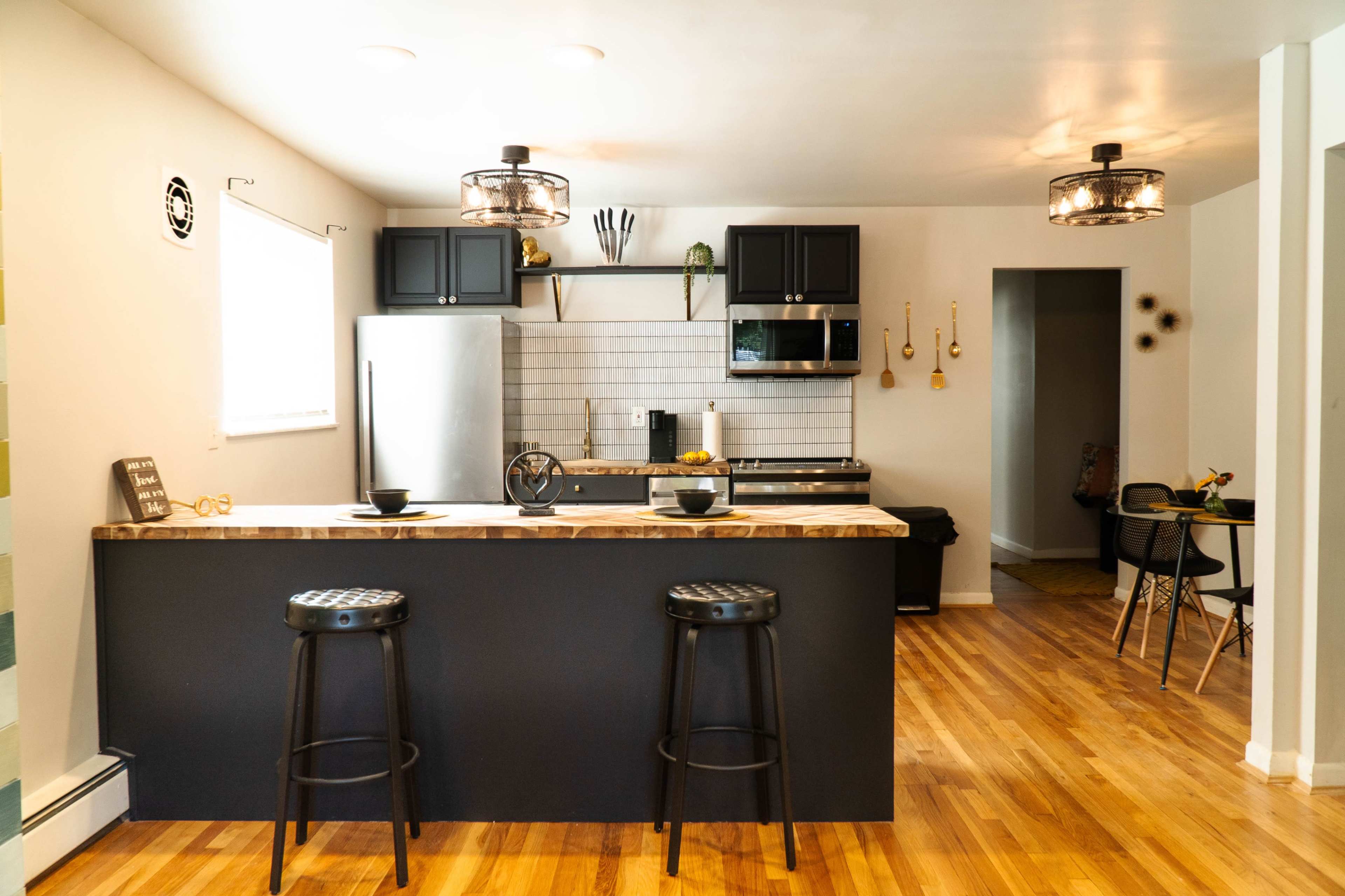 A modern kitchen features dark cabinetry, stainless steel appliances, and a wooden countertop with two bar stools.