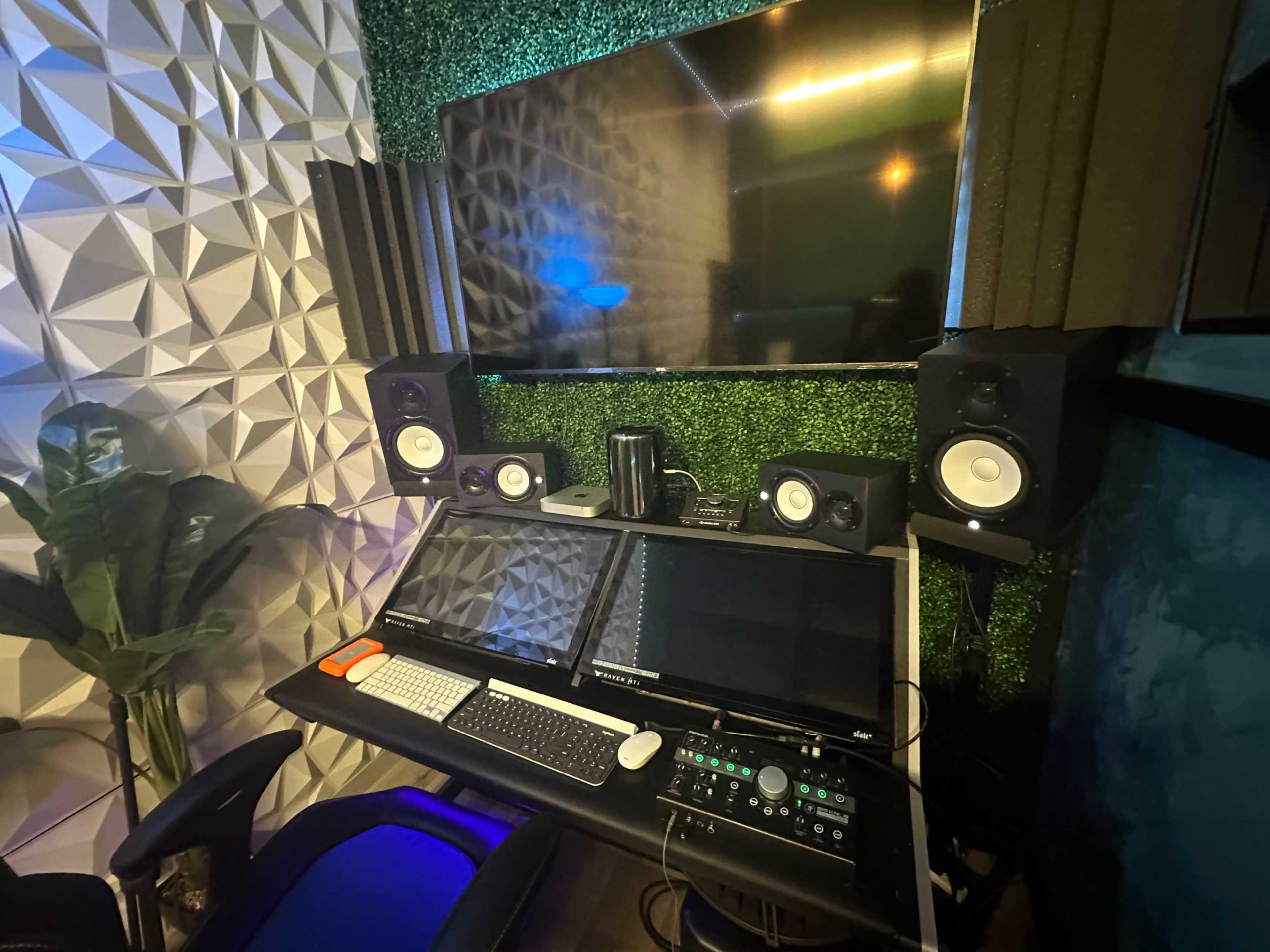 A music production studio setup featuring dual monitors, studio speakers, and soundproofing panels on the walls.