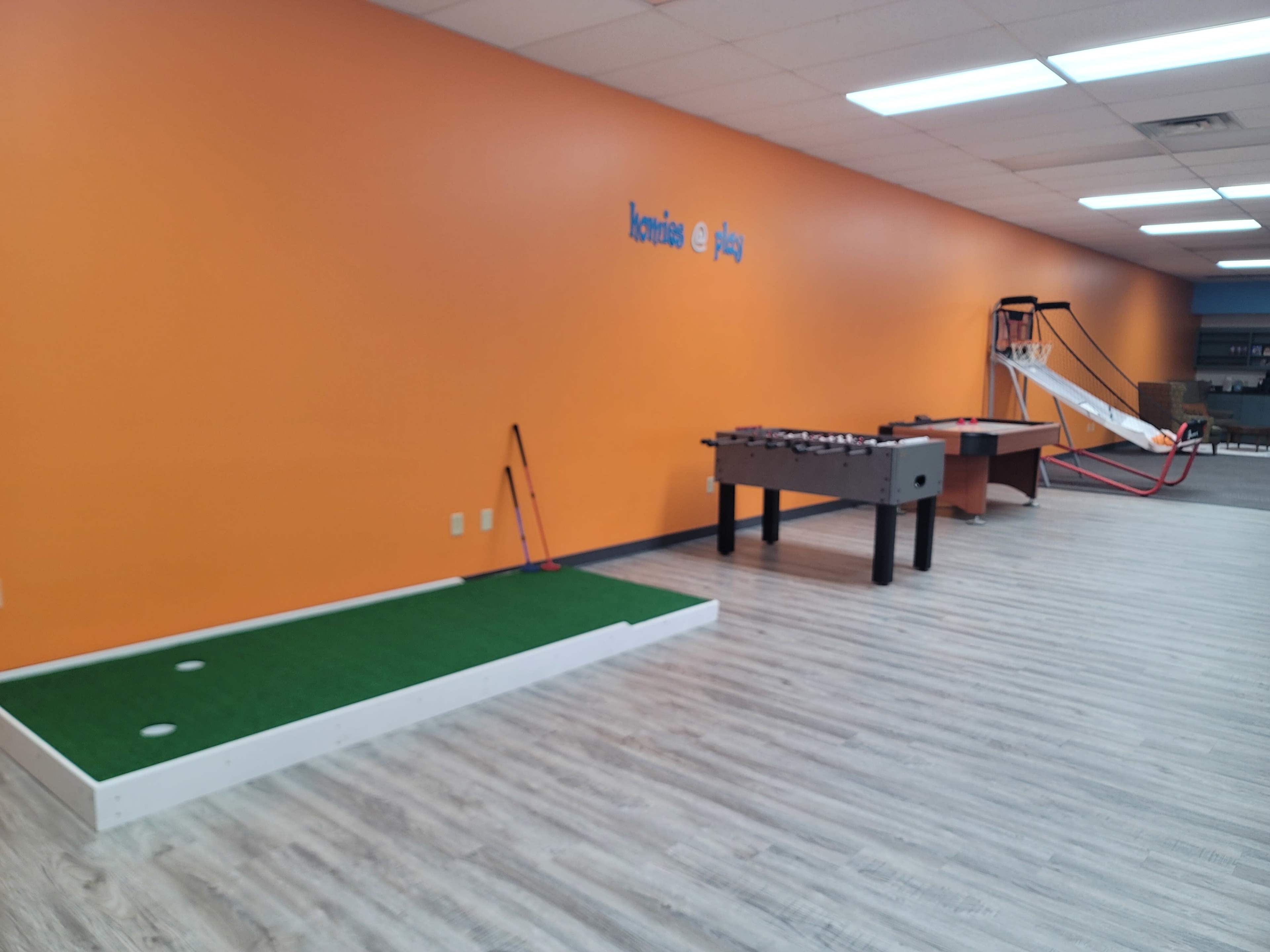 A recreational area with an orange wall featuring a putting green, a foosball table, and a slide.