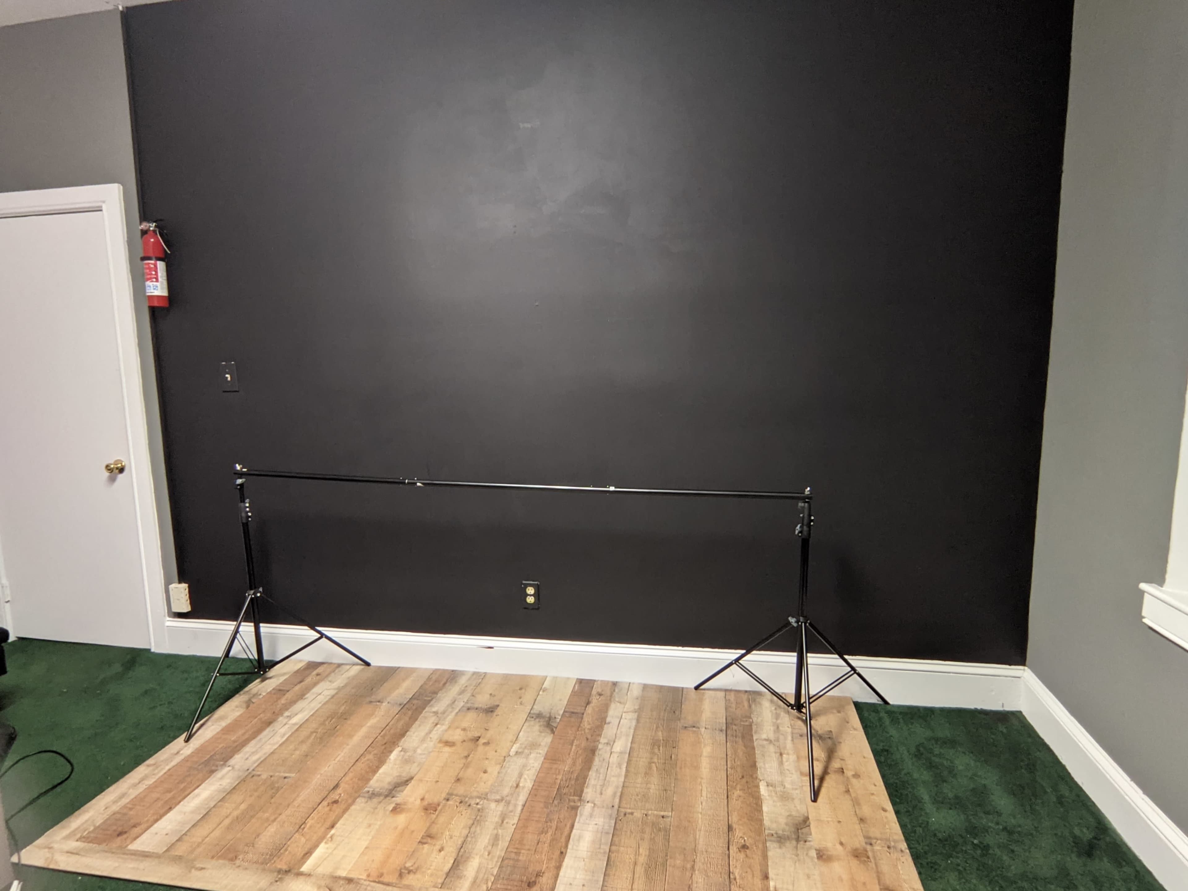 A minimalist setting with a wooden platform in front of a black wall, supported by two metal stands on either side.