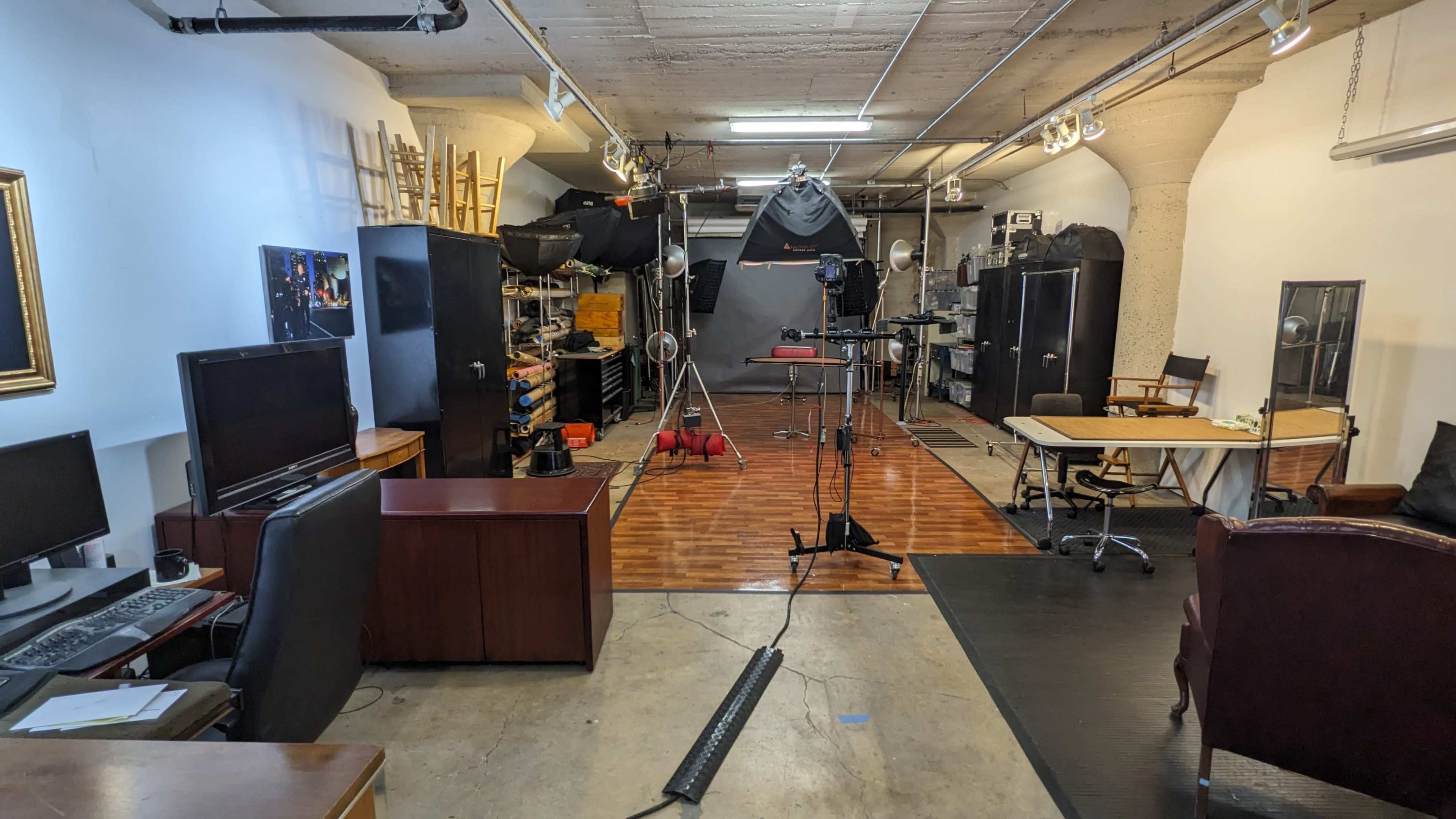 The image shows a spacious studio setup with various equipment, including cameras and lighting, arranged around wooden and concrete flooring.