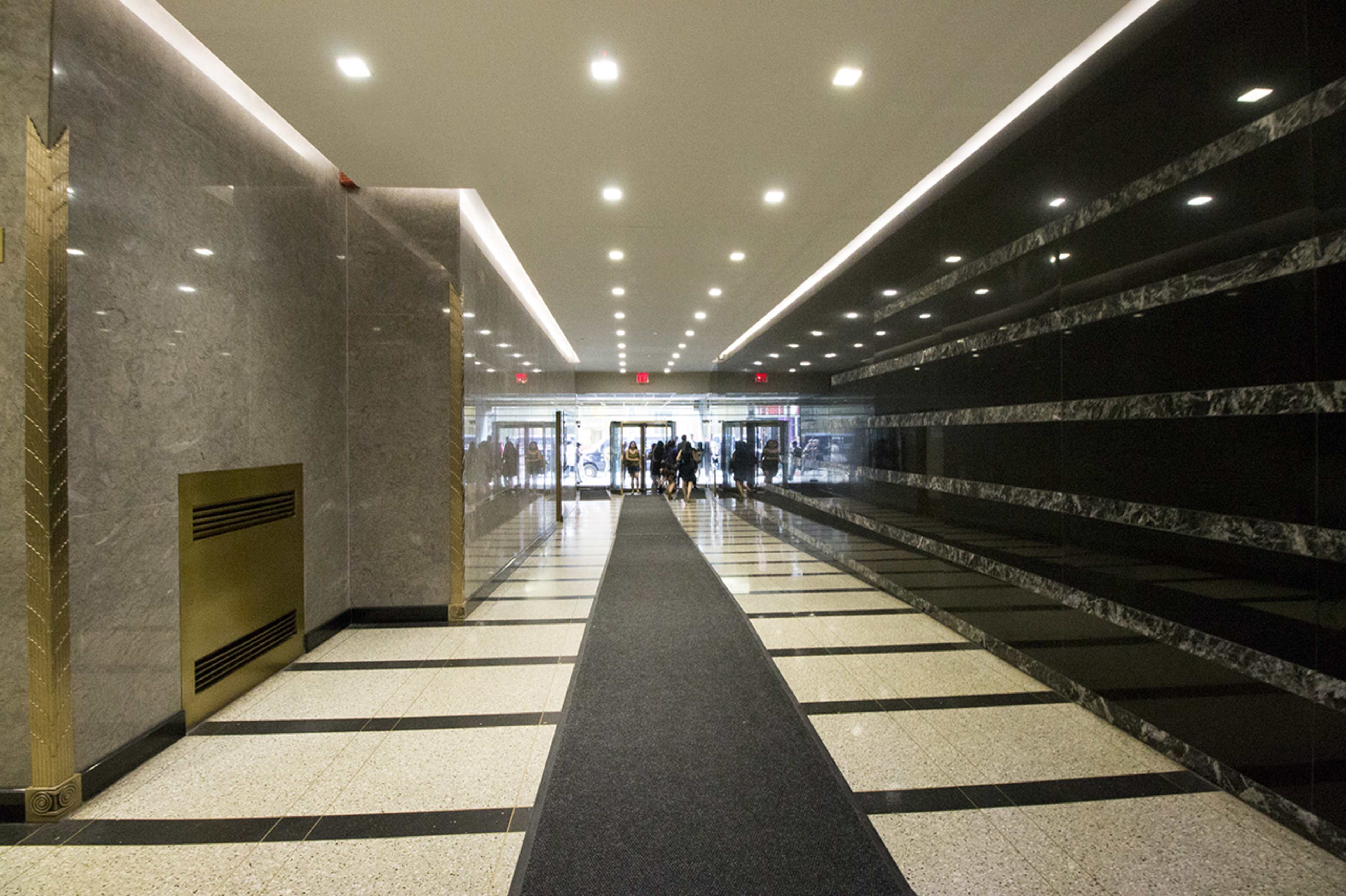 A long, wide corridor with polished marble walls and a patterned floor leads to an entrance illuminated by natural light.