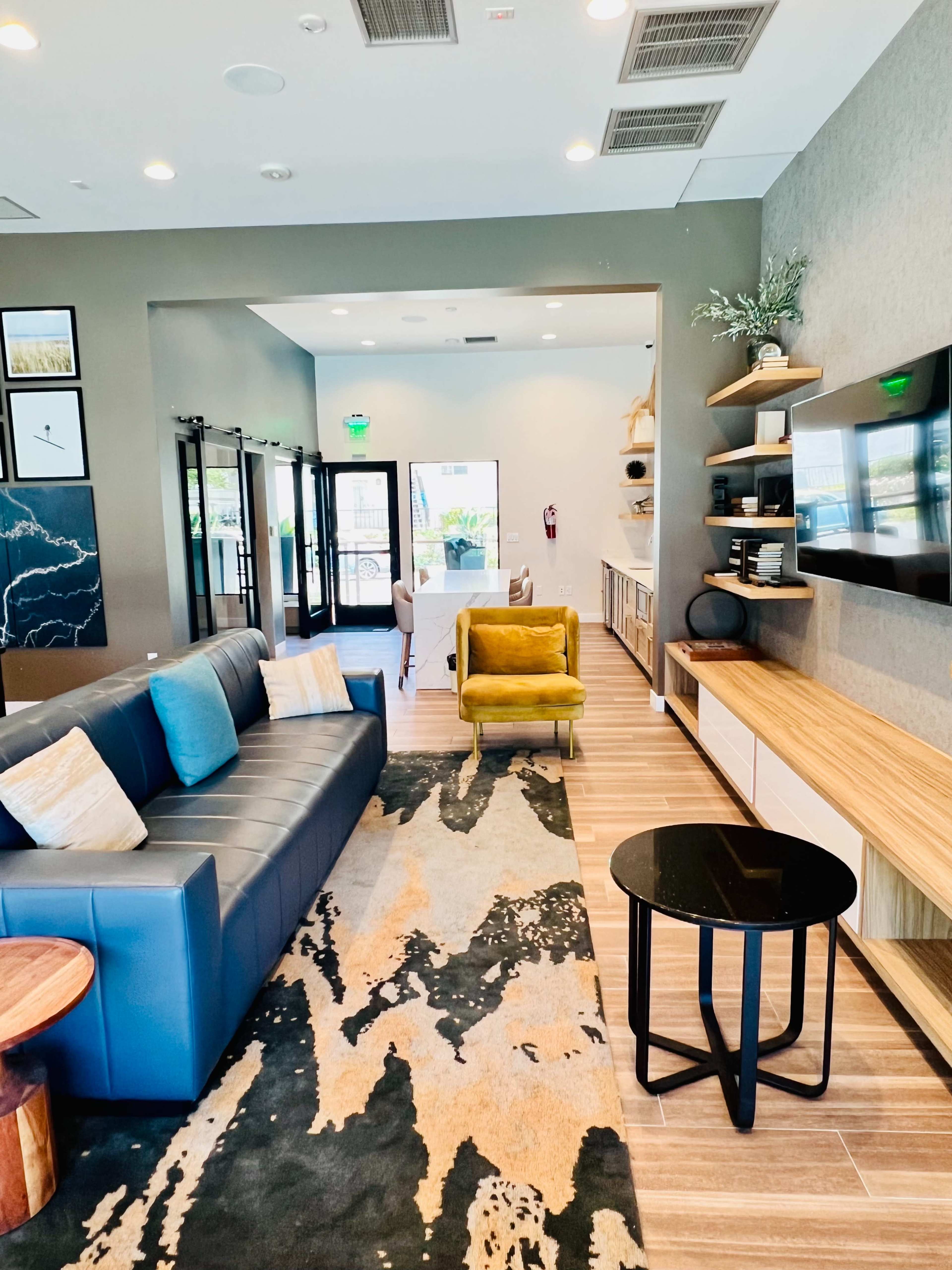 A modern lounge area with a blue sofa, green chair, wooden coffee table, and a wall-mounted TV.