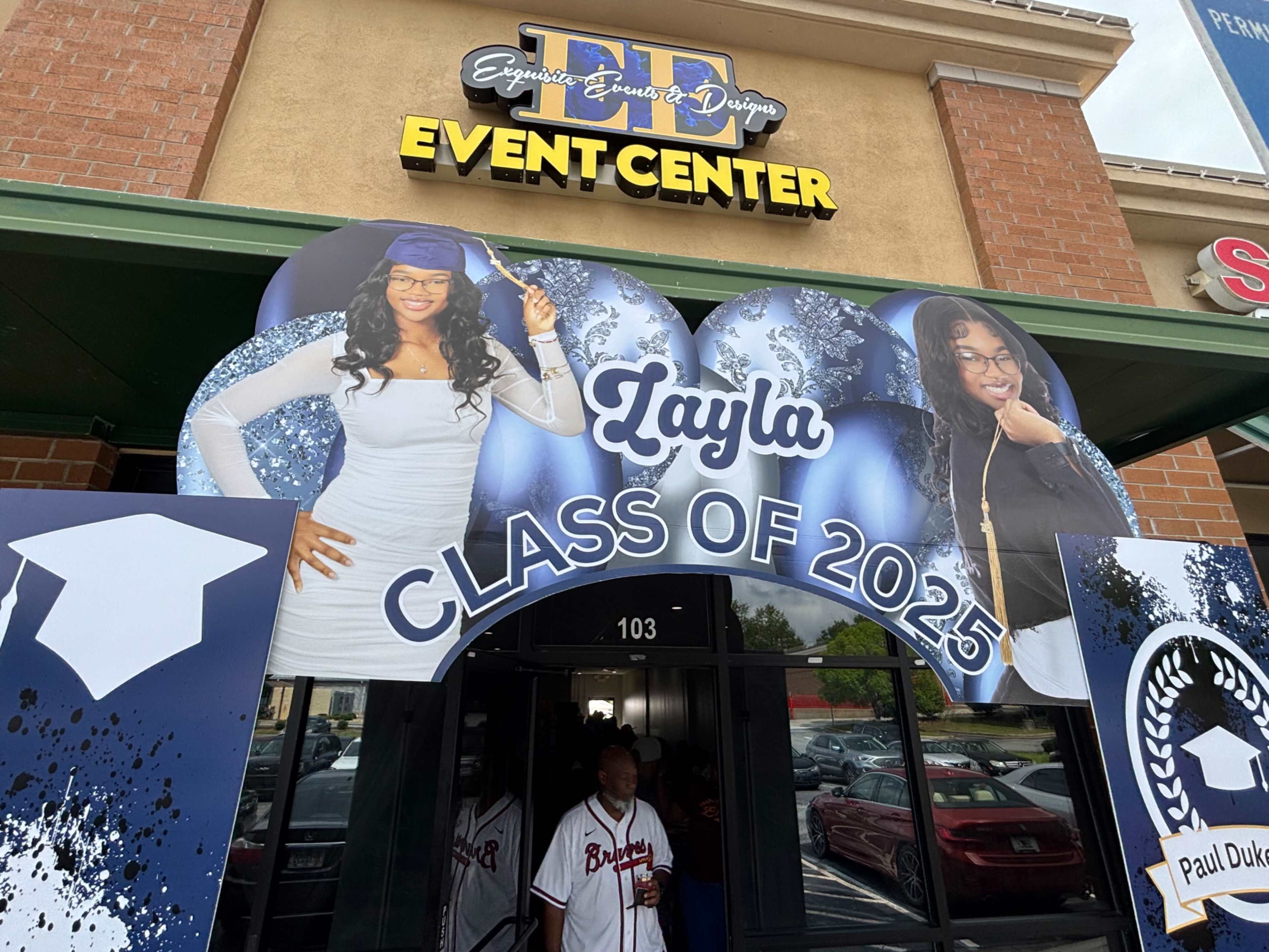 A large banner celebrating the Class of 2025 for a student named Layla is displayed outside an event center, featuring images of two individuals in graduation attire.