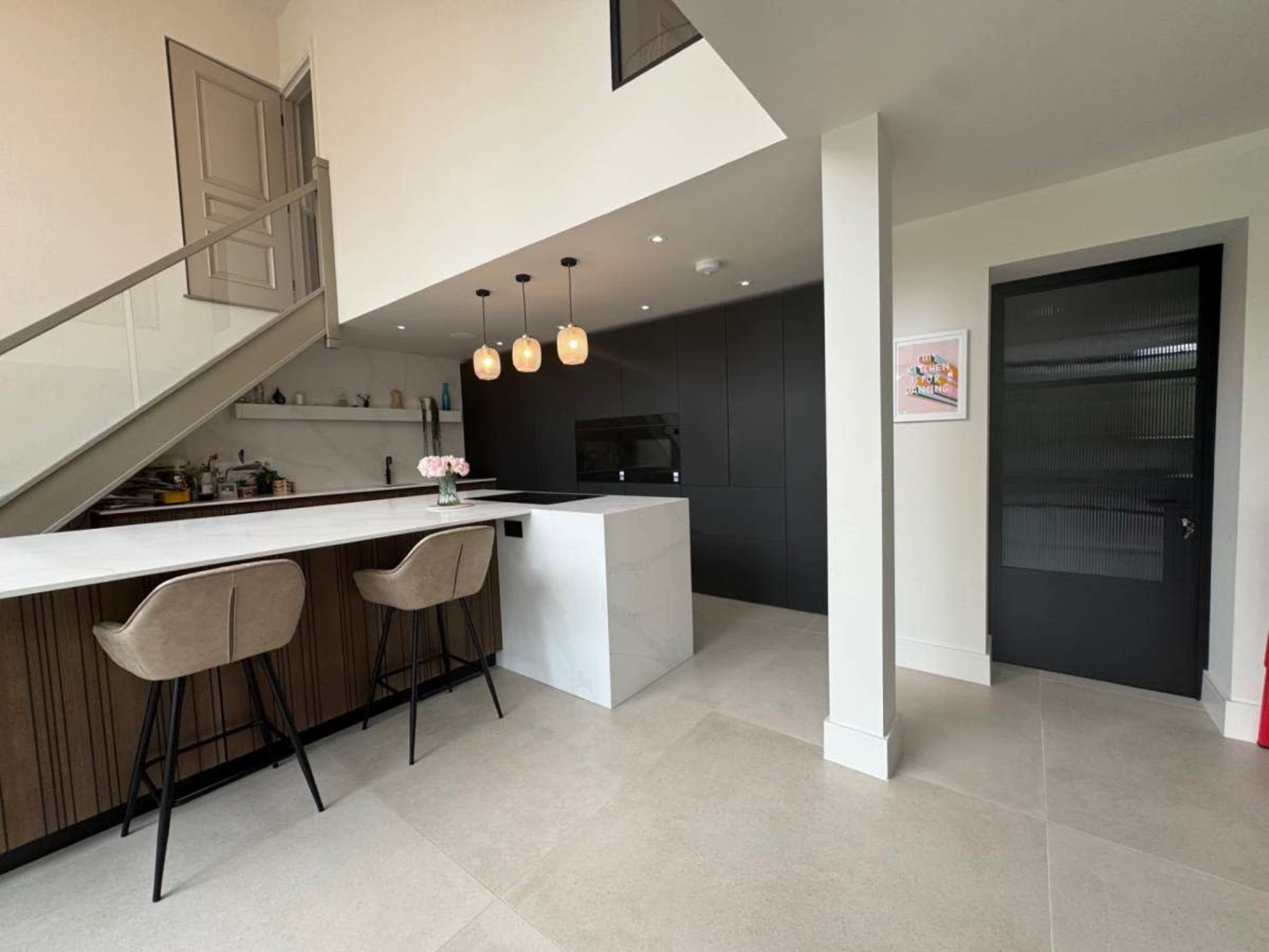 The image shows a modern kitchen with a marble island, wooden cabinetry, and two bar stools situated under pendant lights.
