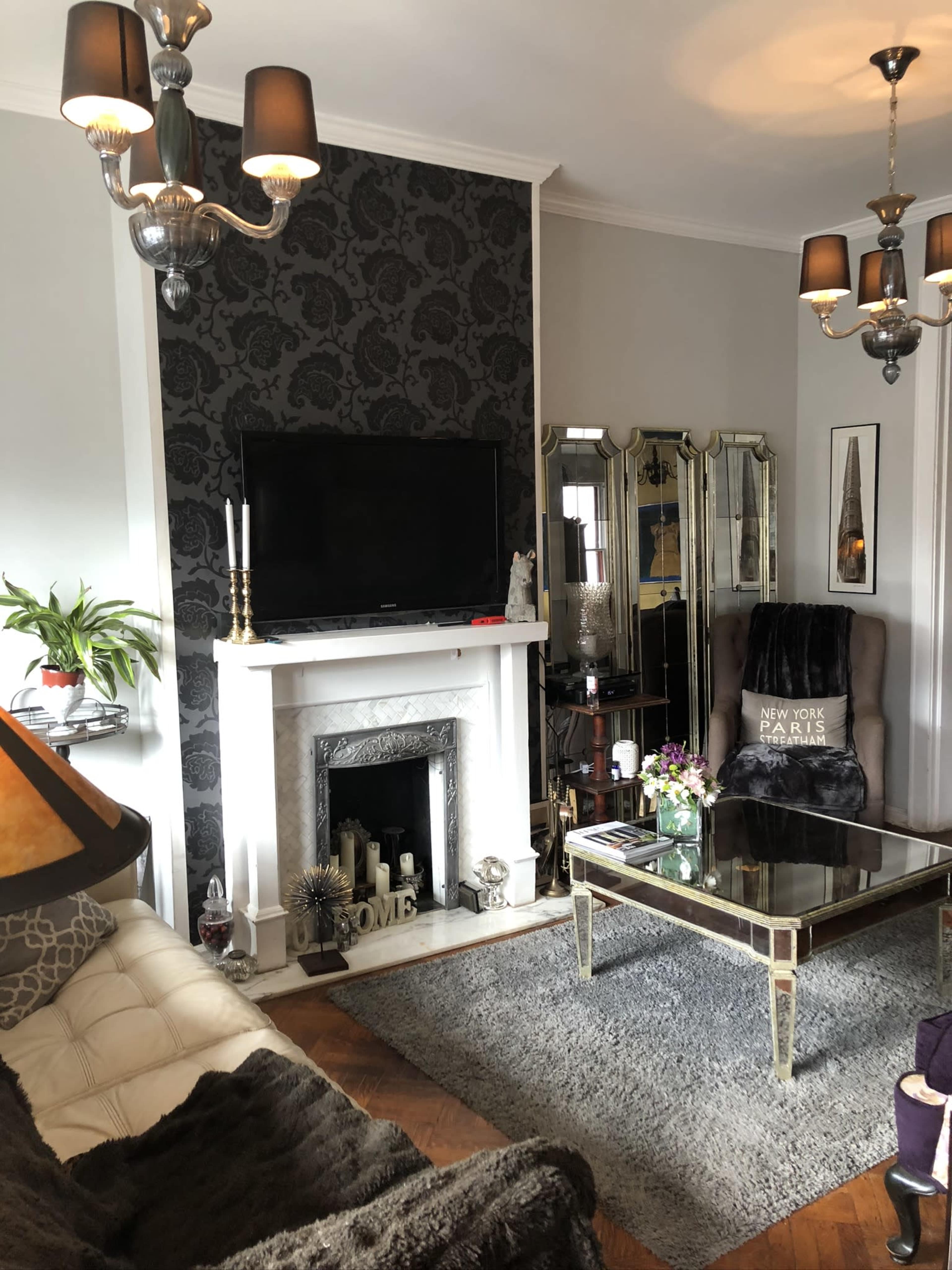 A stylish living room featuring a modern fireplace, a large flat-screen TV, and a mirrored coffee table, with decorative elements including candles and plants.