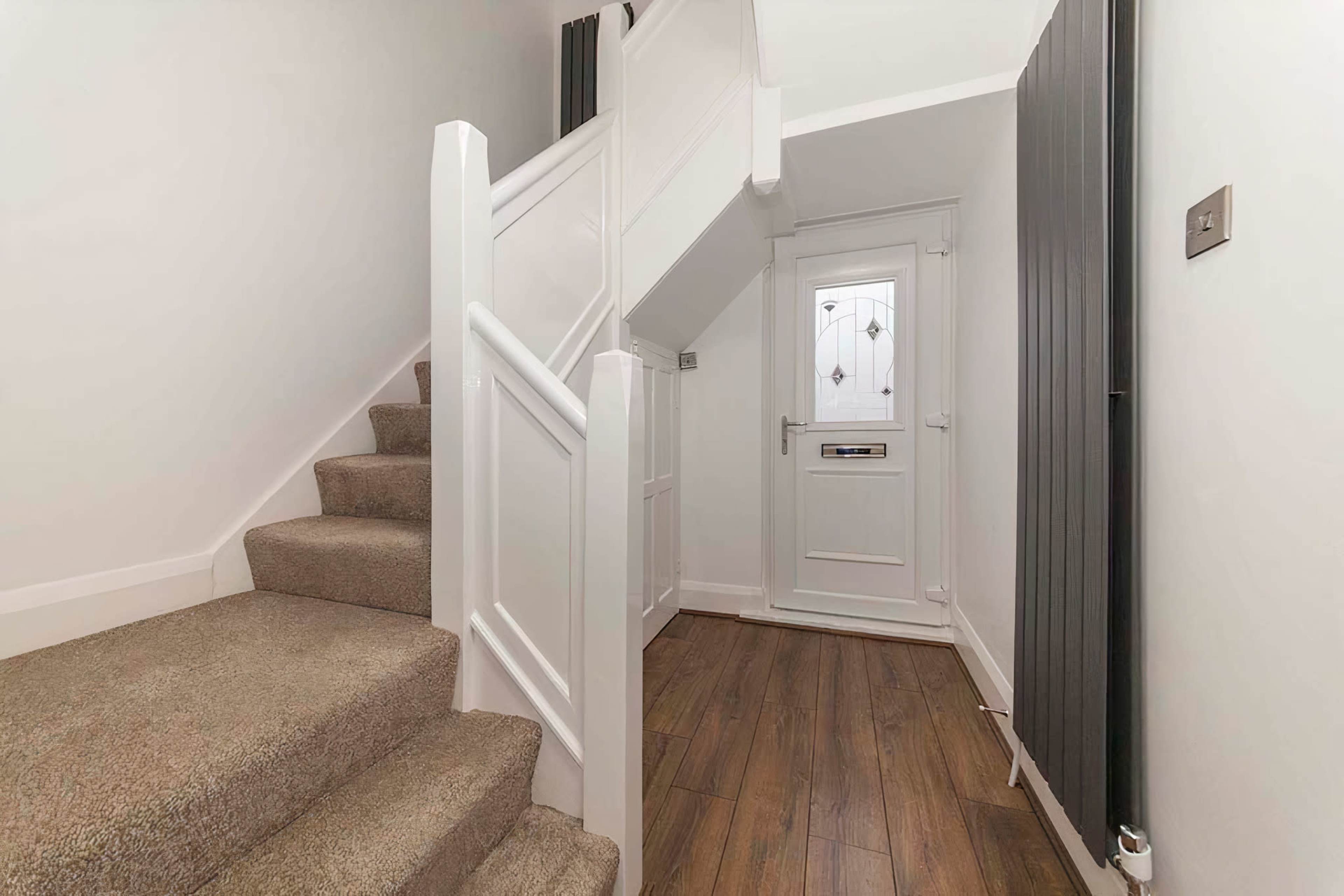 A well-lit hallway featuring a staircase with carpeted steps and a door with decorative glass panels at the end.