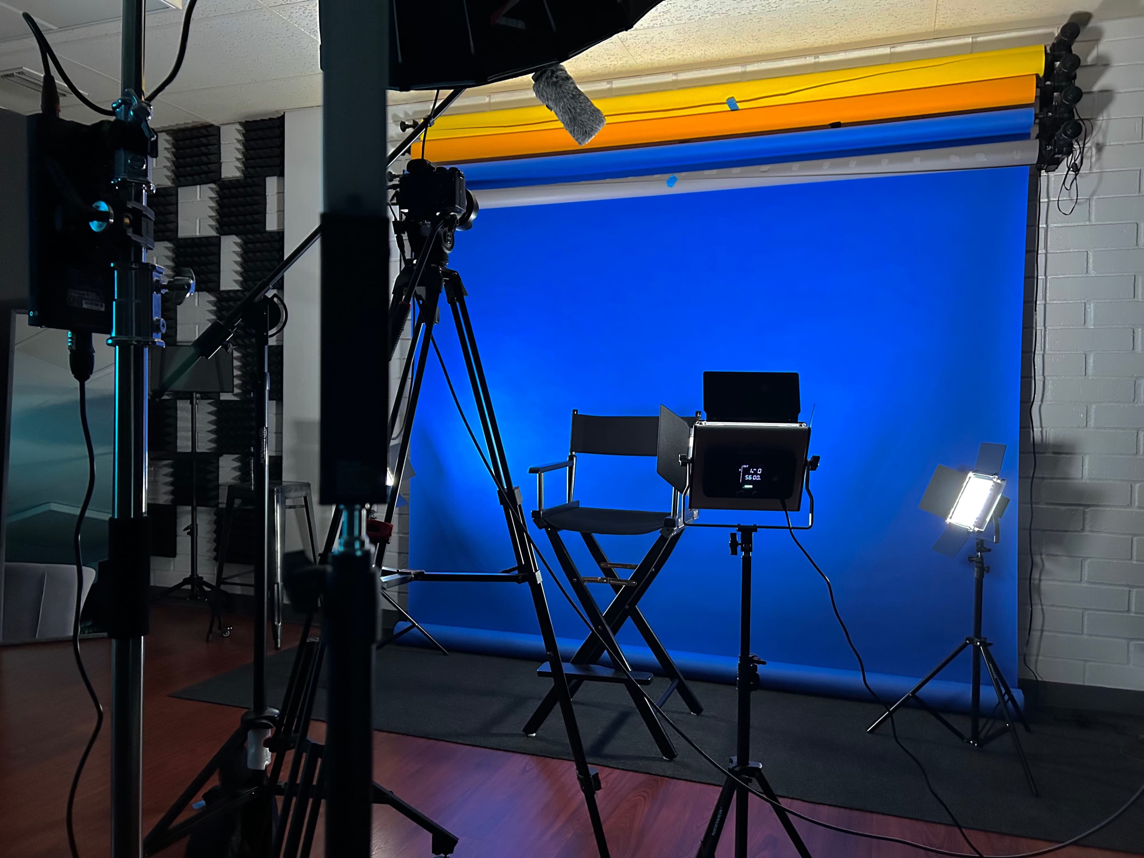 A photography studio setup with a blue backdrop, studio lights, and a director's chair.