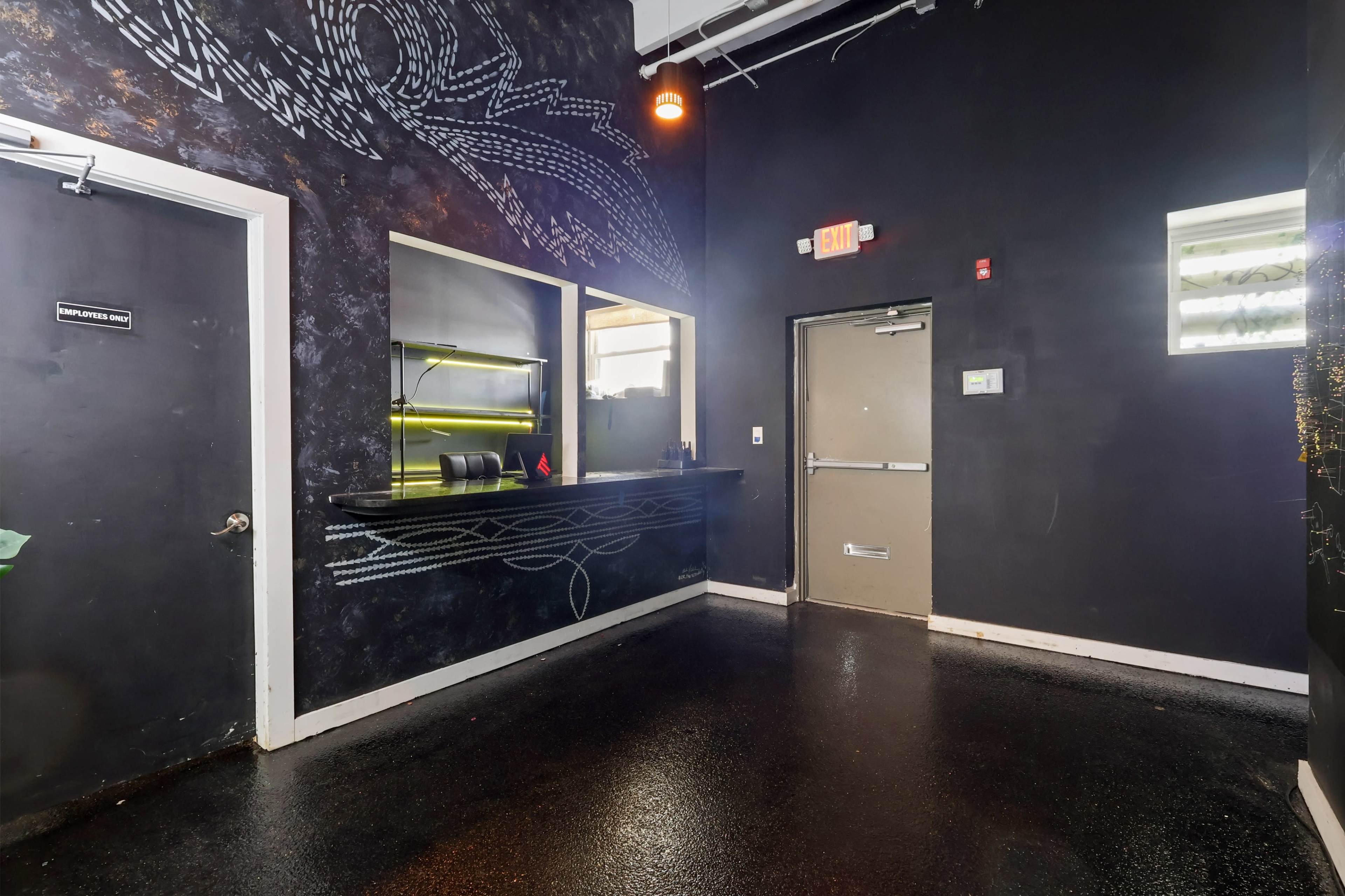The image shows a dimly lit reception area with dark walls, a small service counter, and a door leading to another room.