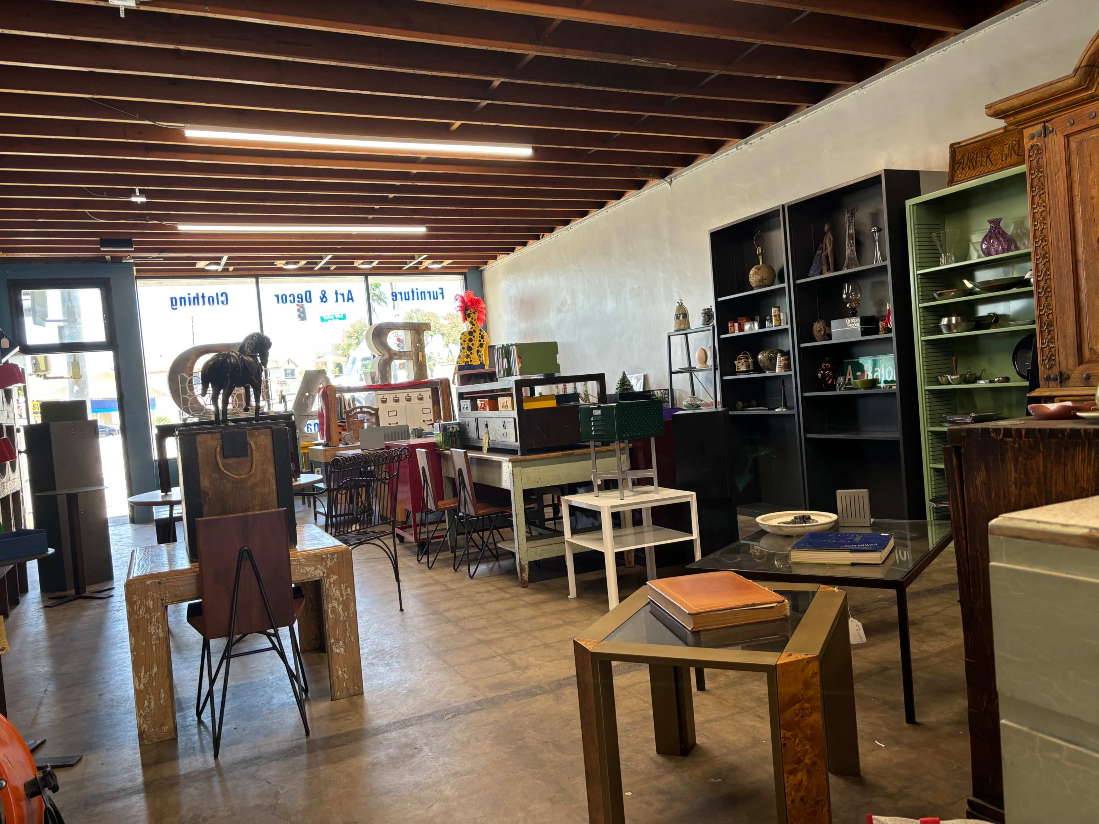 A vintage furniture store interior with various pieces displayed on wooden and metal furniture under exposed beam ceilings.