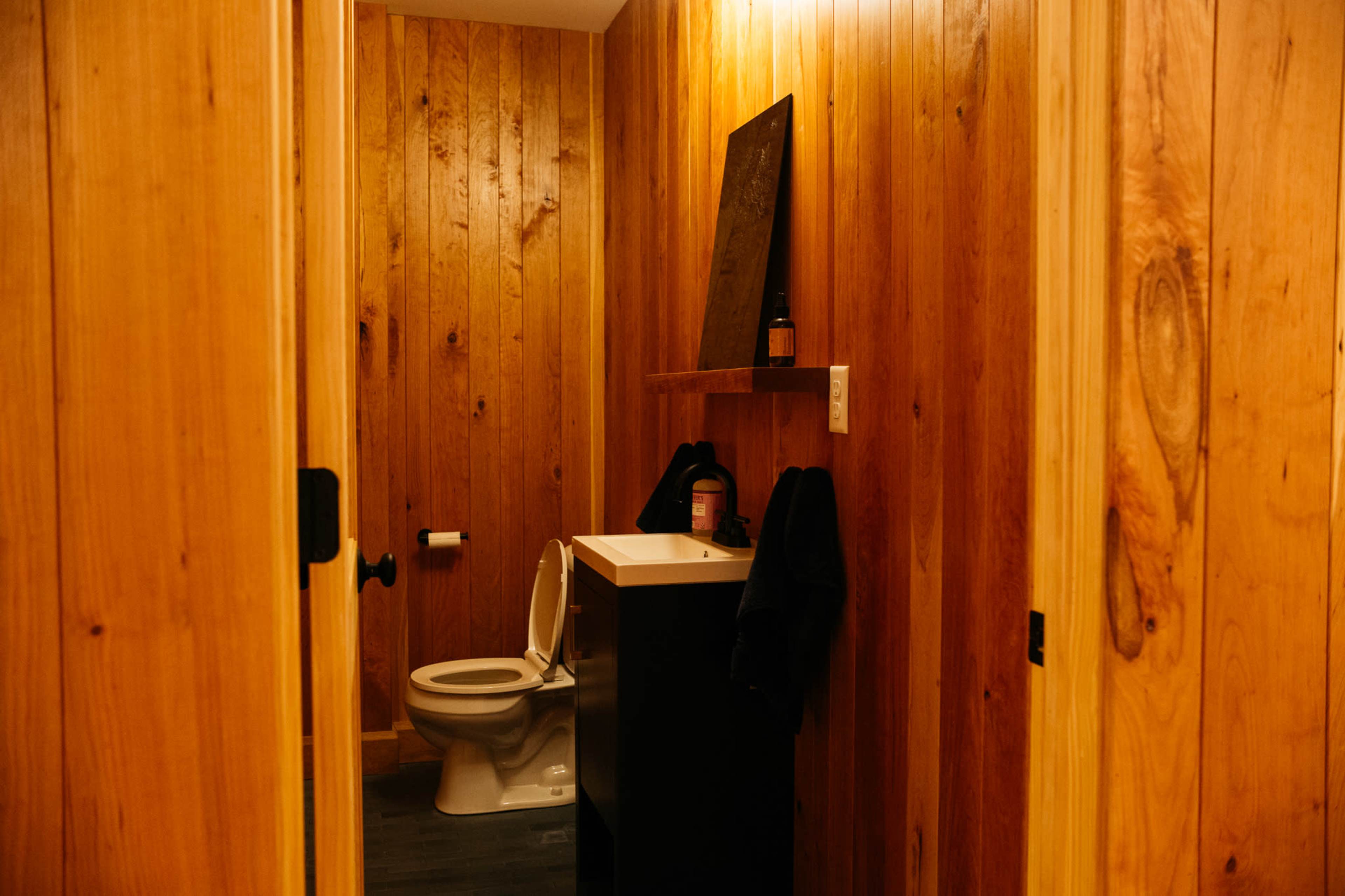 A small bathroom with wooden walls, featuring a toilet and a sink on a cabinet.