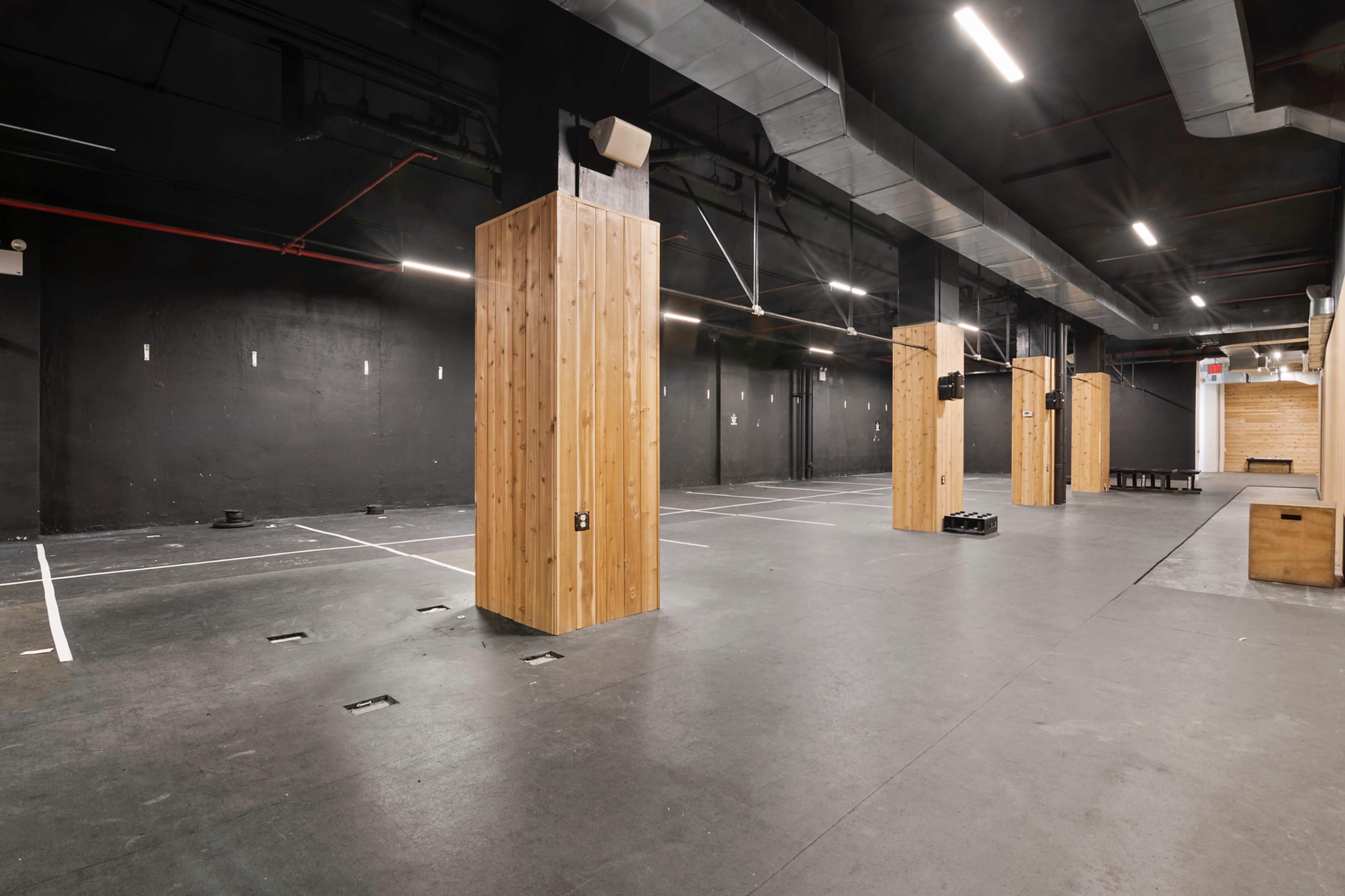The image shows a large, empty indoor space with wooden pillars and a dark ceiling.