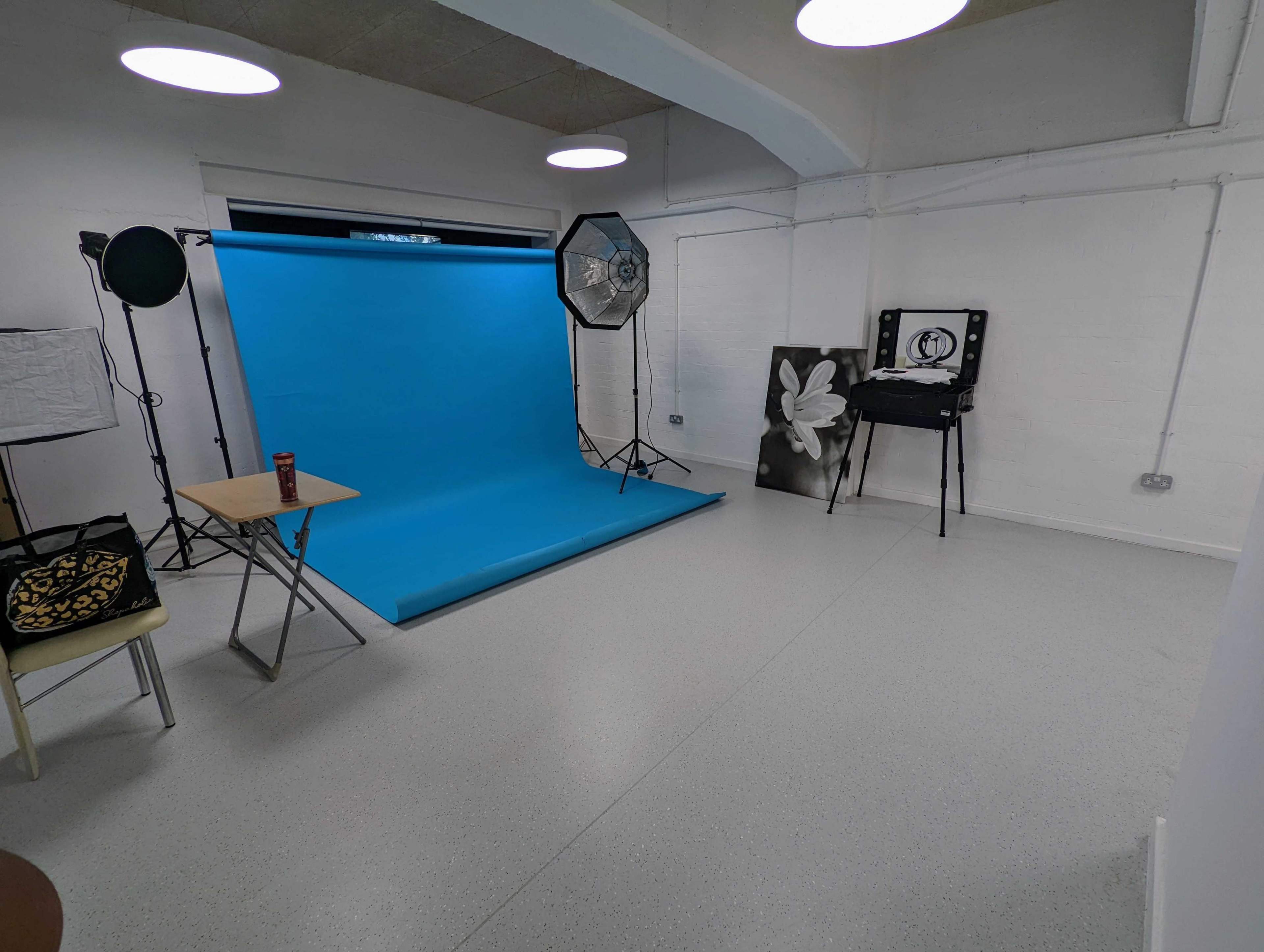 A photography studio with a blue backdrop, softbox lighting, and a table set up in a sparsely furnished room.