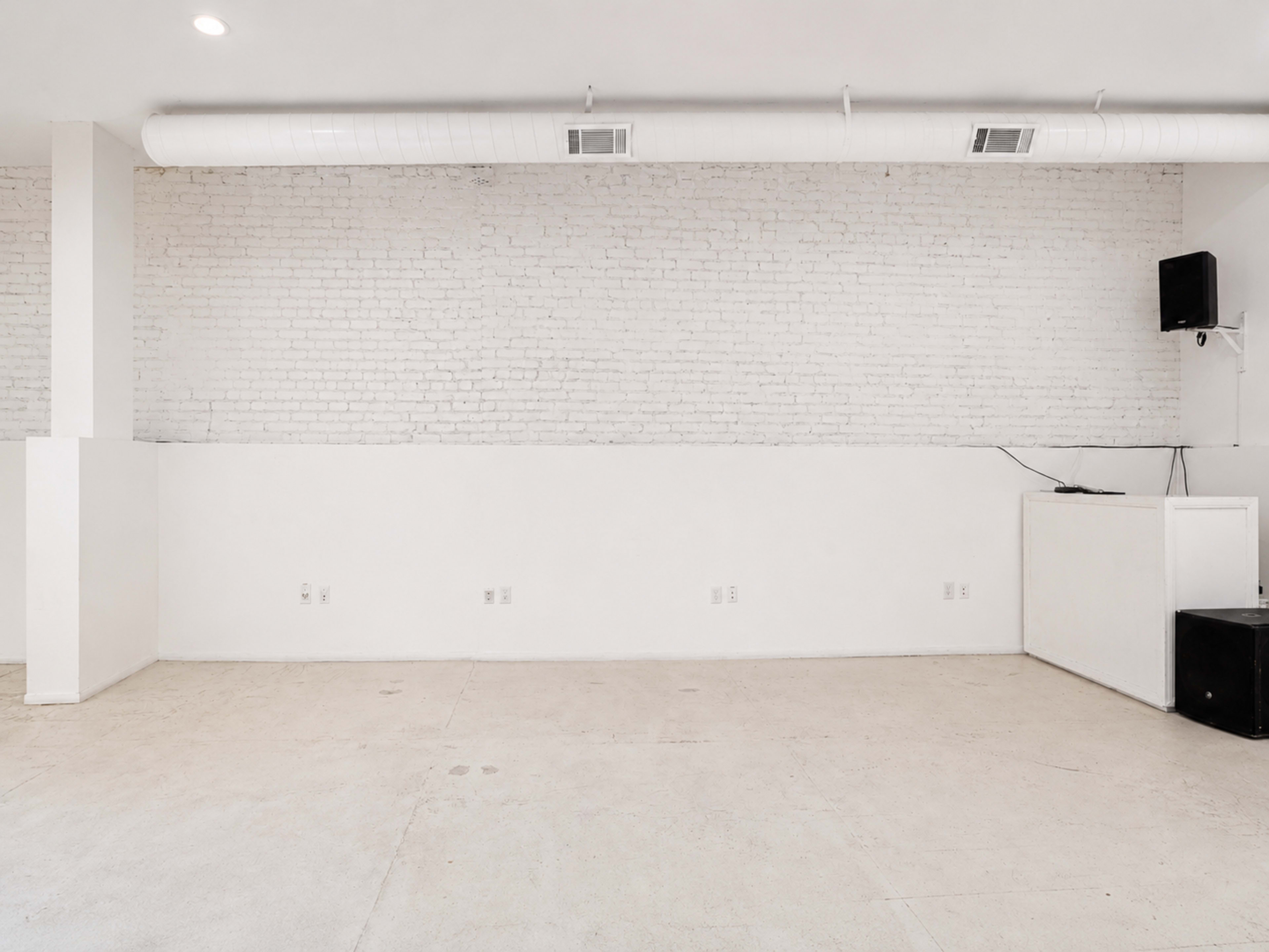 The image shows an empty room with white brick walls and a light-colored floor, featuring minimal furnishings and equipment.