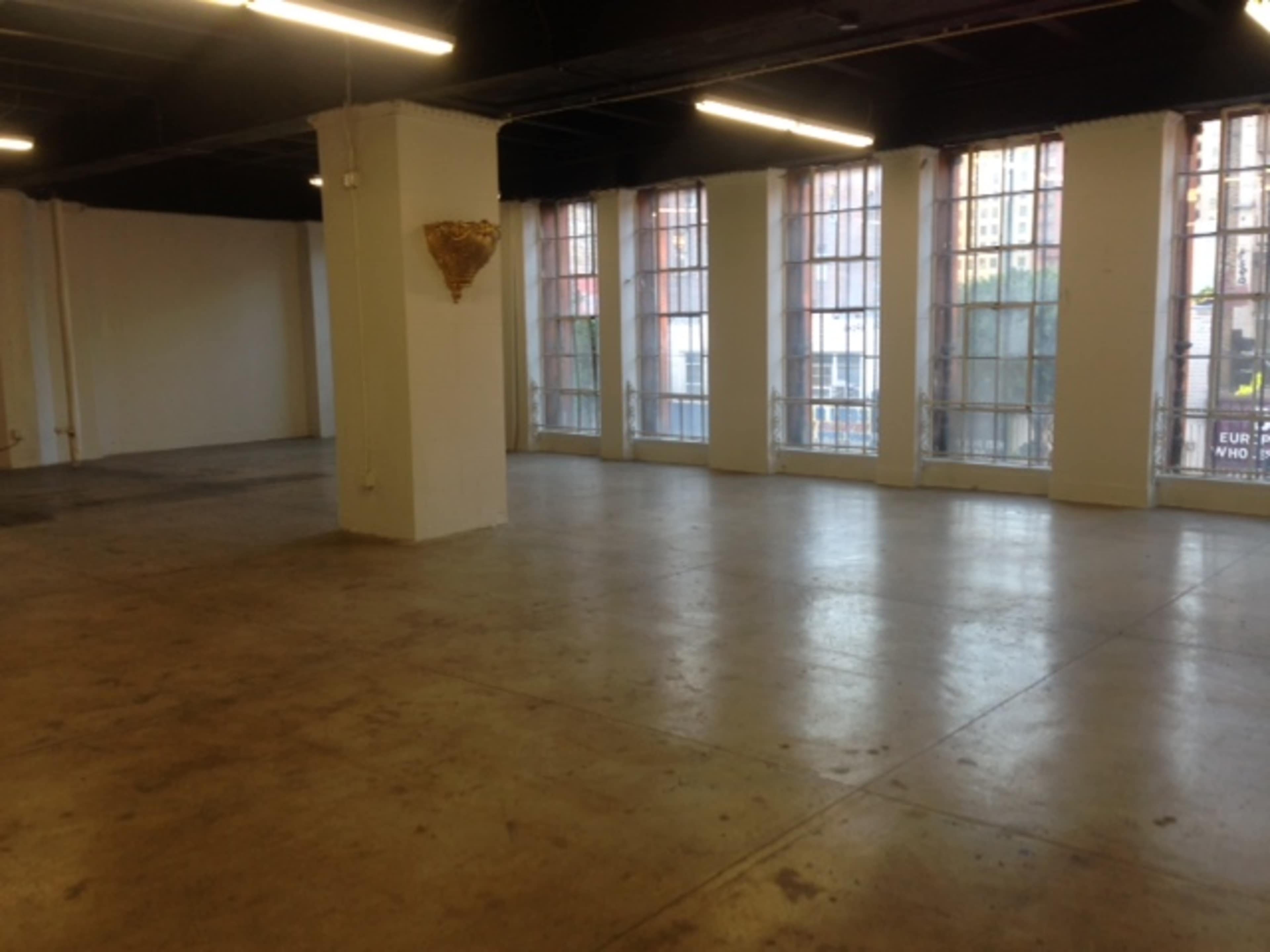A large, empty room with concrete floors and large windows along one wall.