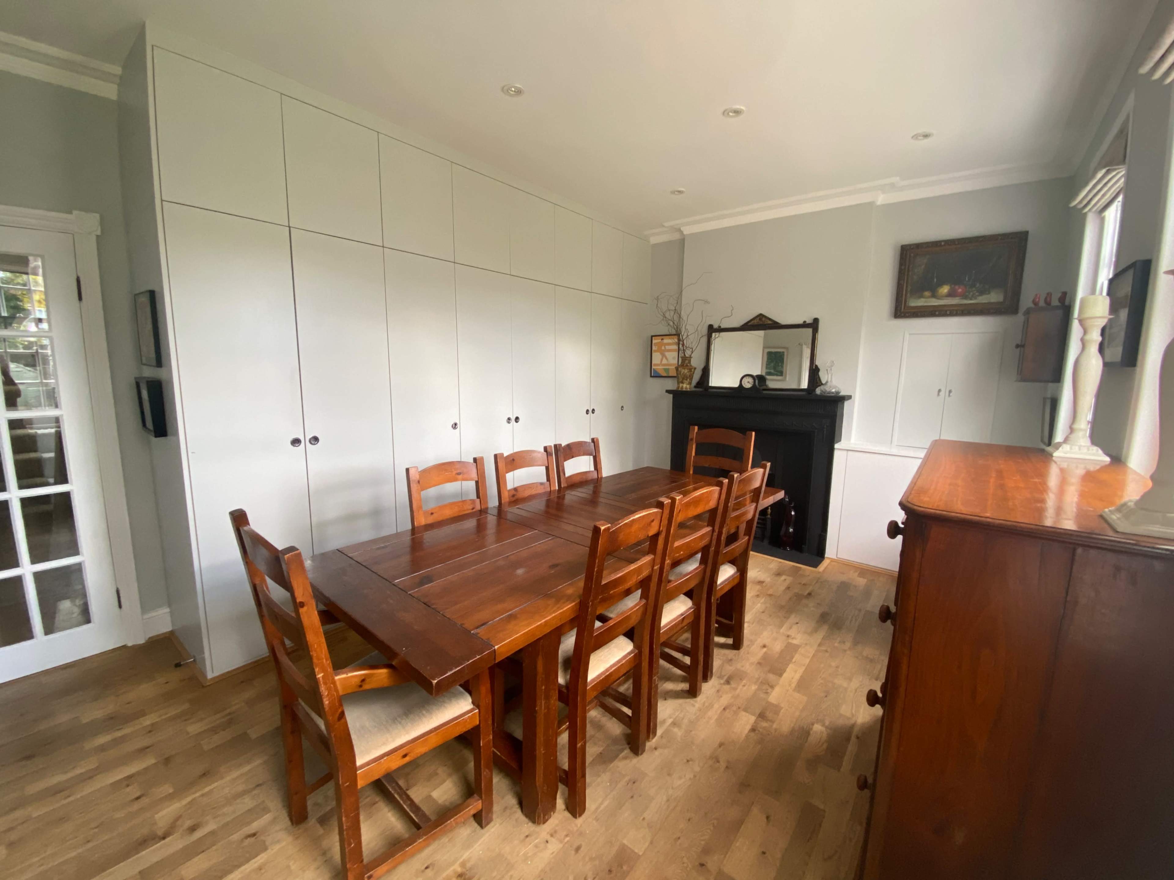 A dining room features a wooden table surrounded by eight chairs, with built-in cabinets and a black fireplace along one wall.