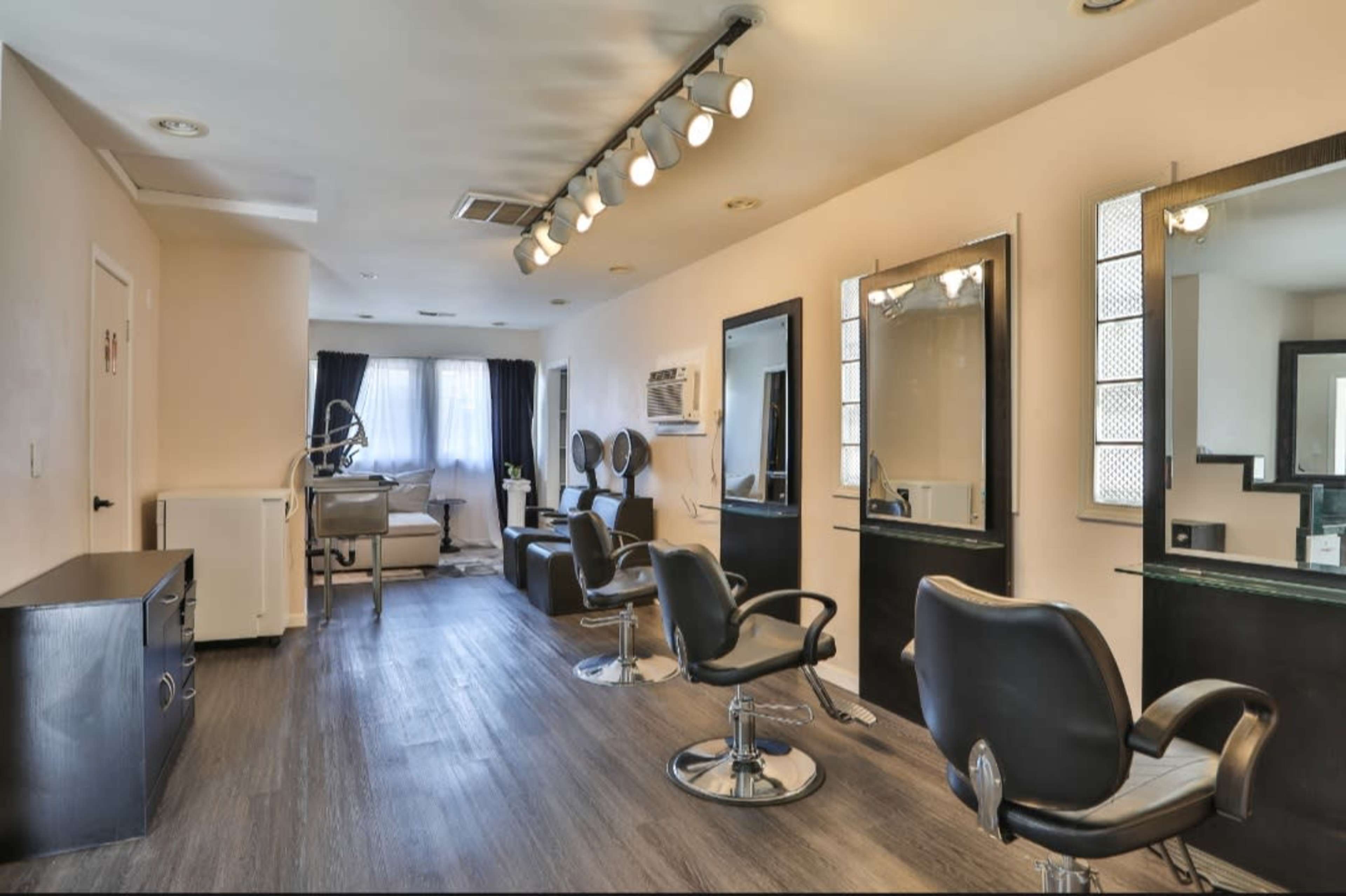 A hair salon with black stylist chairs, mirrors, and a work area in a well-lit room.