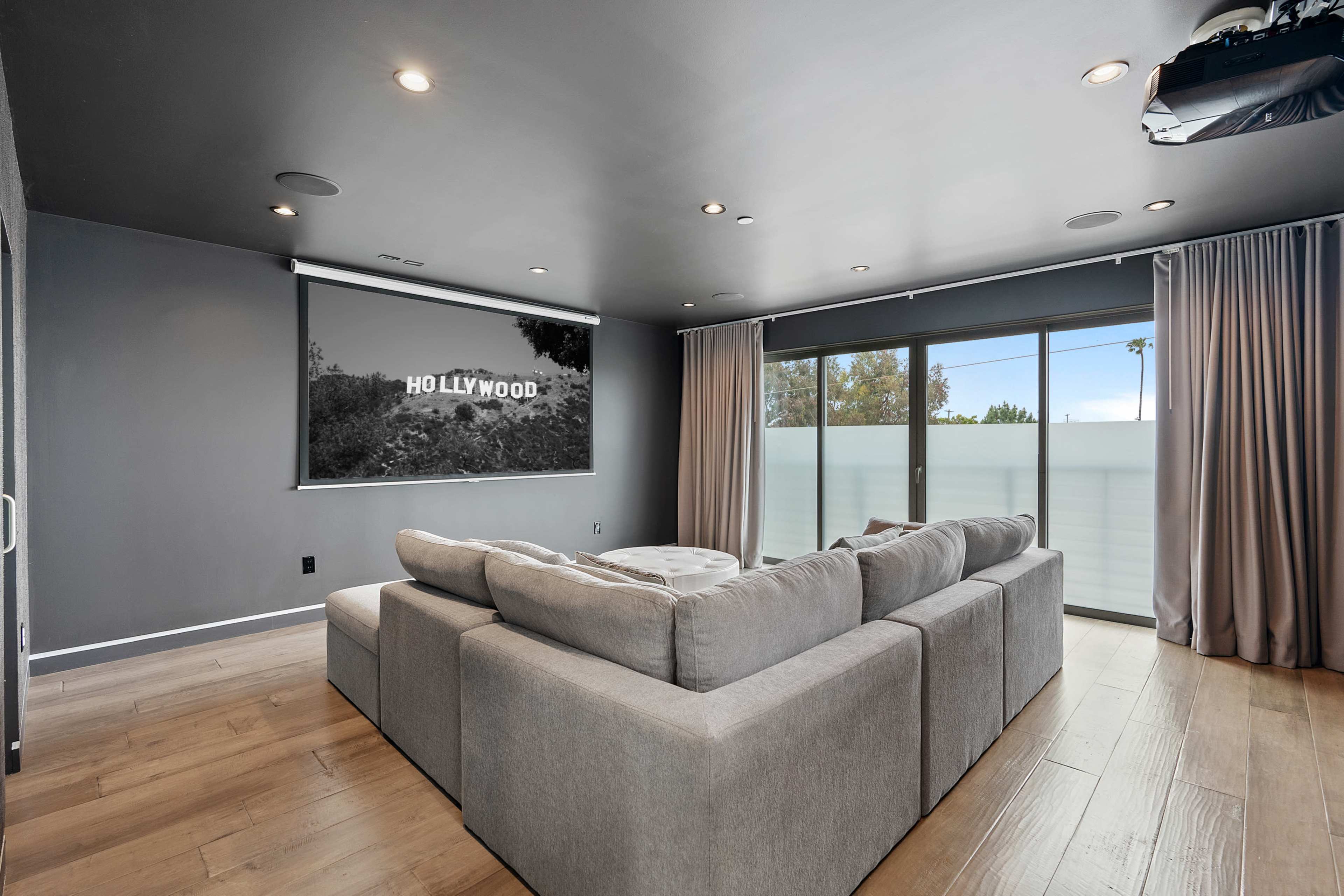 The living room features a large gray sectional sofa facing a projection screen with a view of the Hollywood sign.
