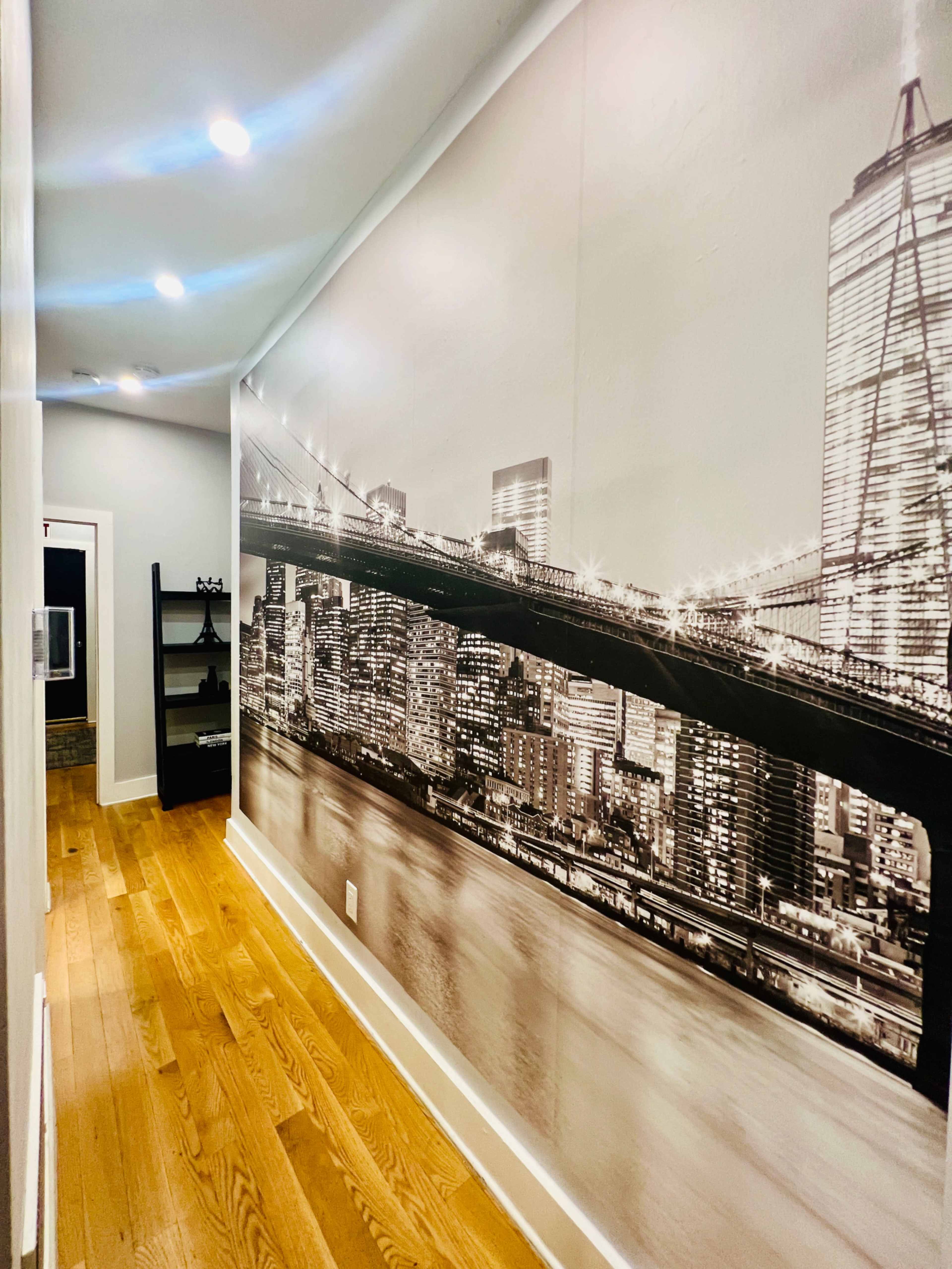 A hallway features a large black-and-white mural of a city skyline with a bridge reflected in water.