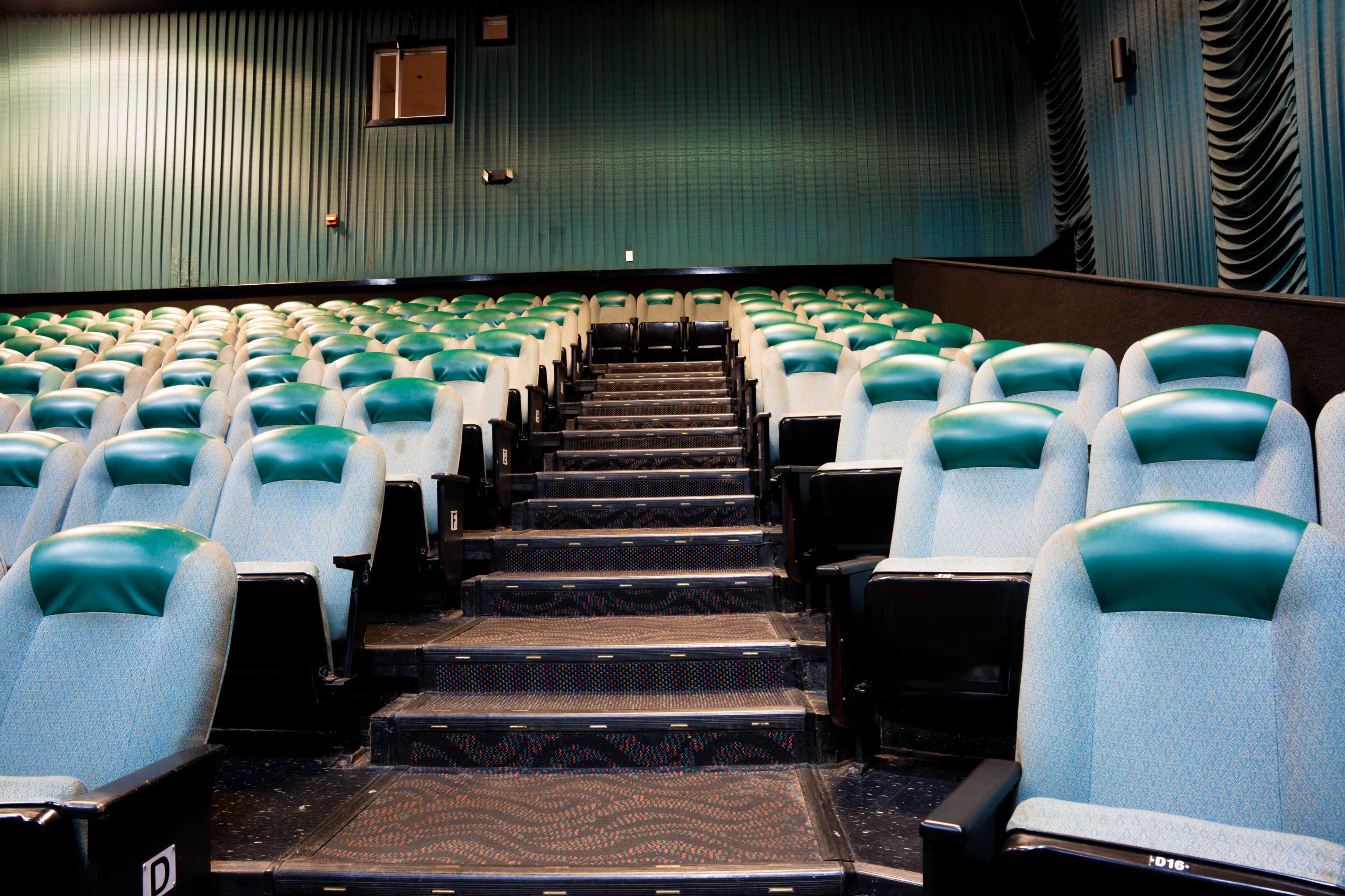 A partially empty theater with green and blue upholstered seats arranged in rows, leading up a staircase.