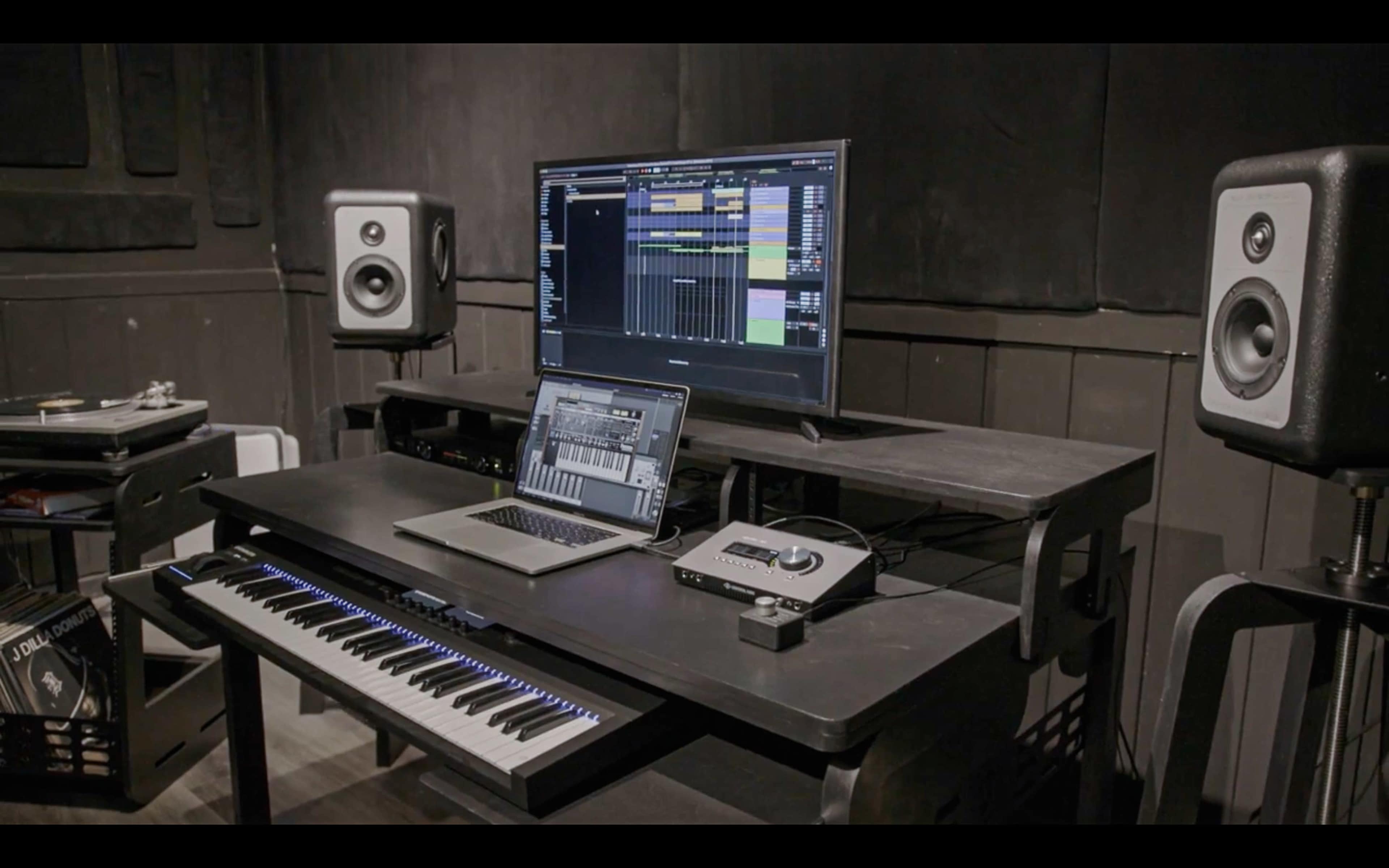 A music production workspace features a keyboard, computer monitors, and audio equipment arranged on a sleek desk.