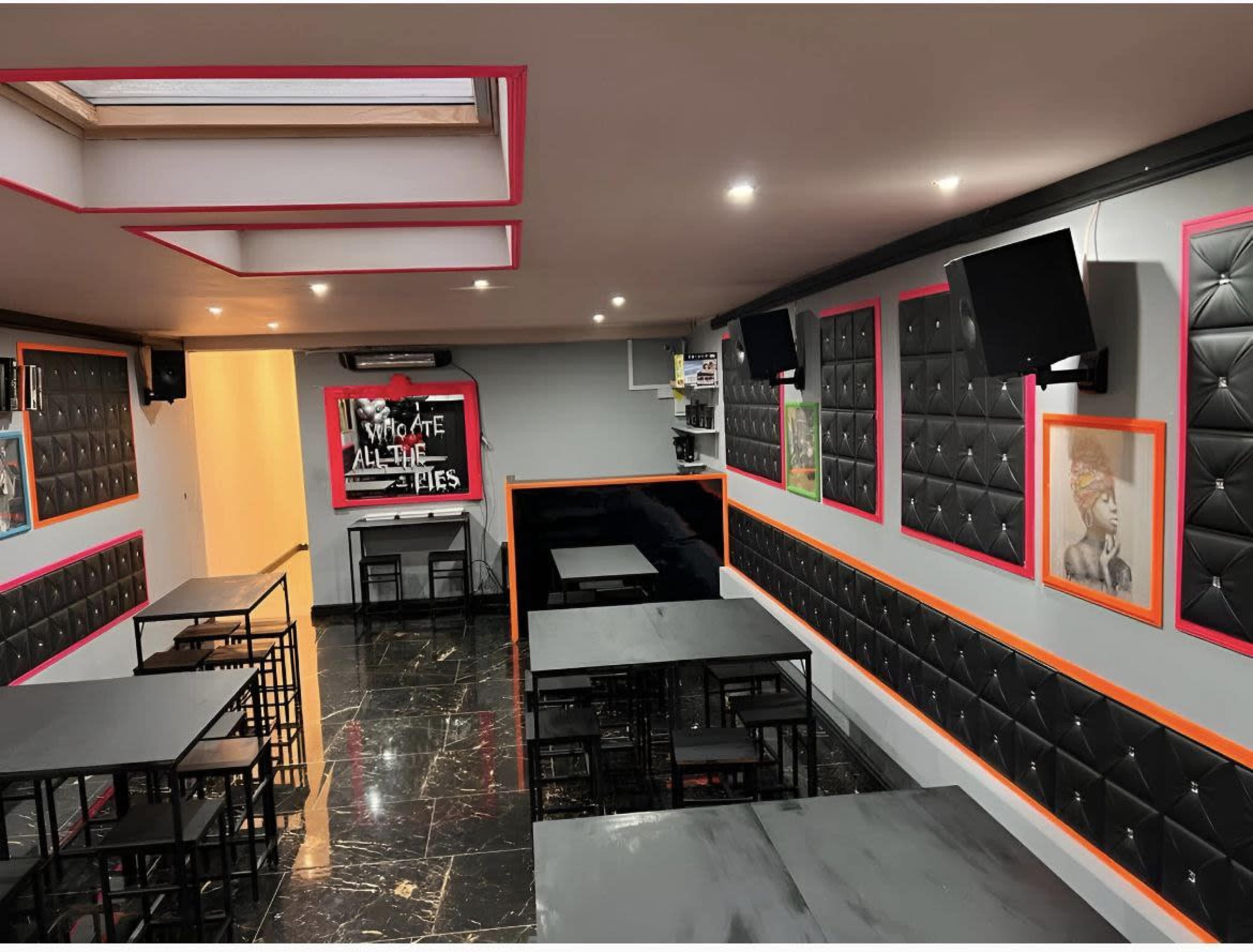 A contemporary dining area with black upholstered walls, multiple flat-screen TVs, and tables arranged in a modern style.
