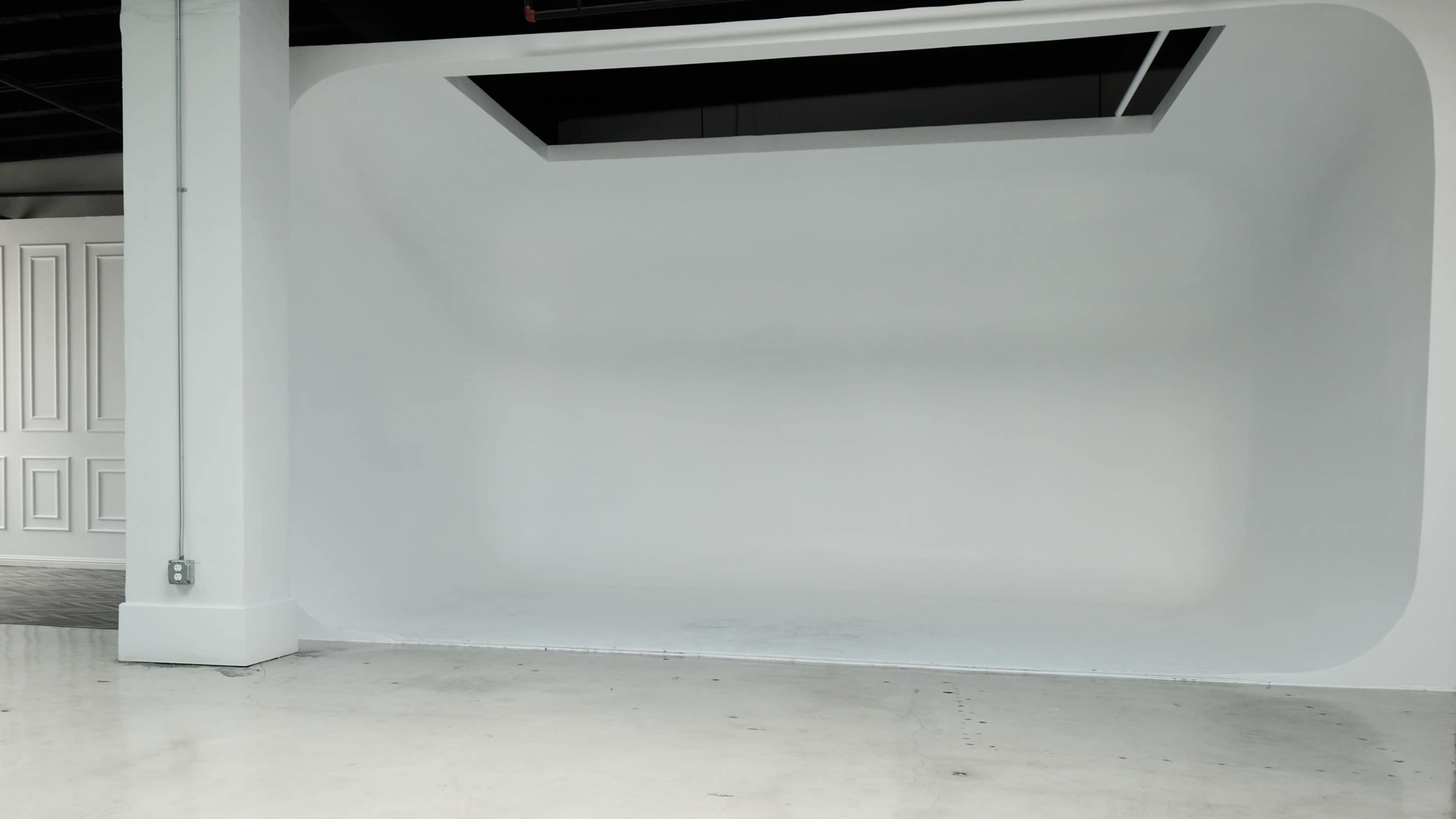 A spacious, bare studio with white walls and a seamless backdrop.