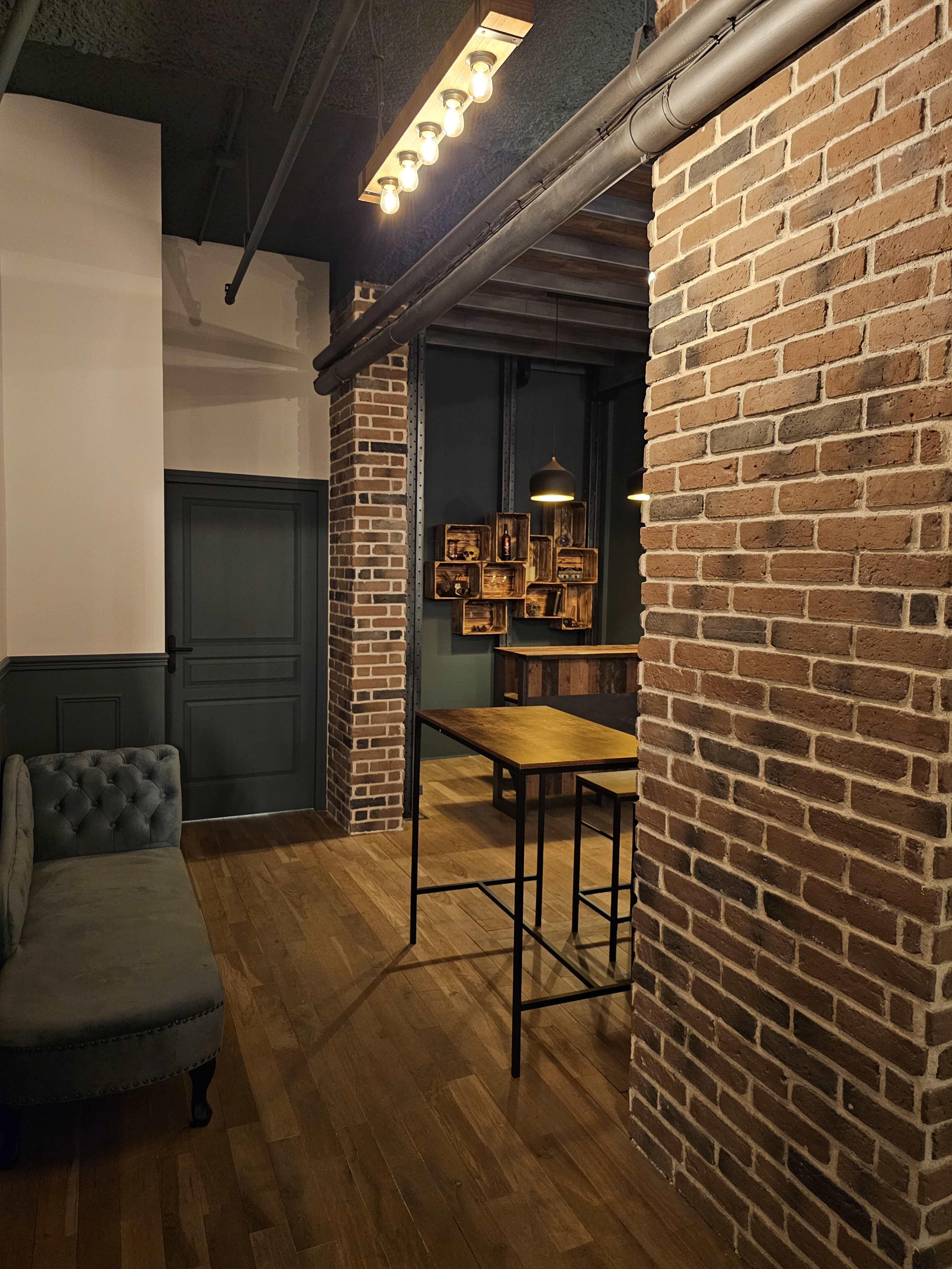 A narrow hallway features exposed brick walls, a wooden floor, a small table, and a dark door at the far end.
