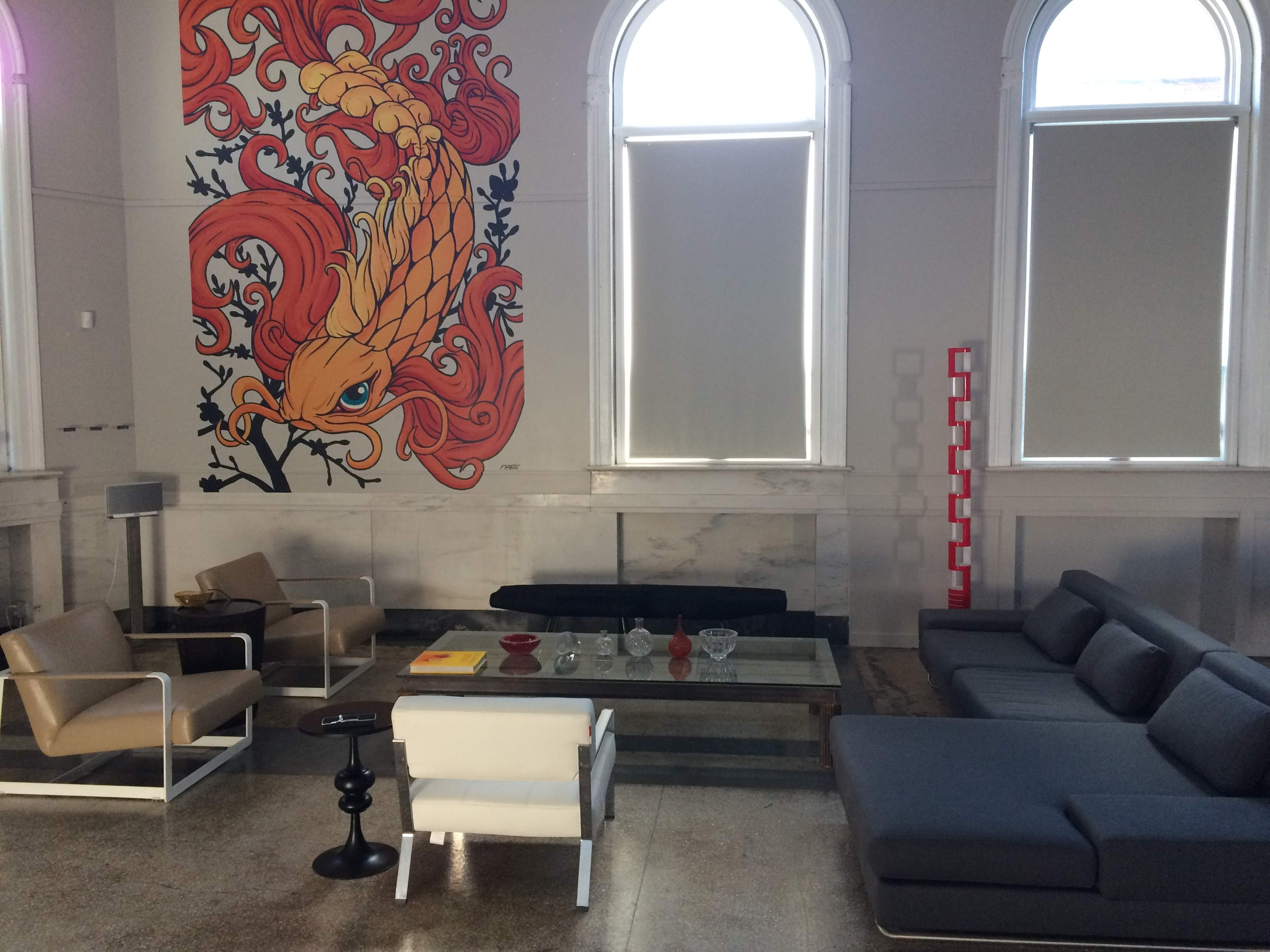 A modern living room featuring a large mural of a colorful bird on the wall, contemporary furniture including a sectional sofa and armchairs, and a minimalist coffee table.