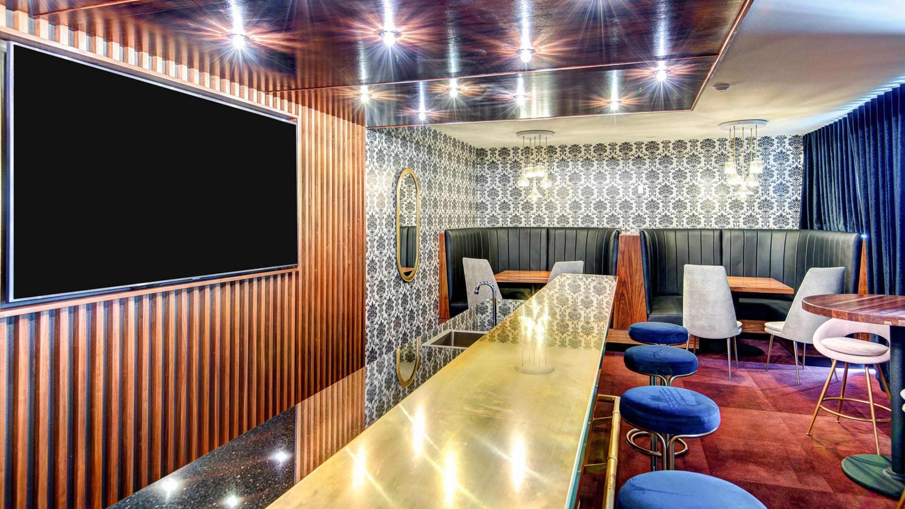 A modern lounge area featuring a bar with a brass countertop, several high-backed booths, and a large wall-mounted screen in an elegant setting.