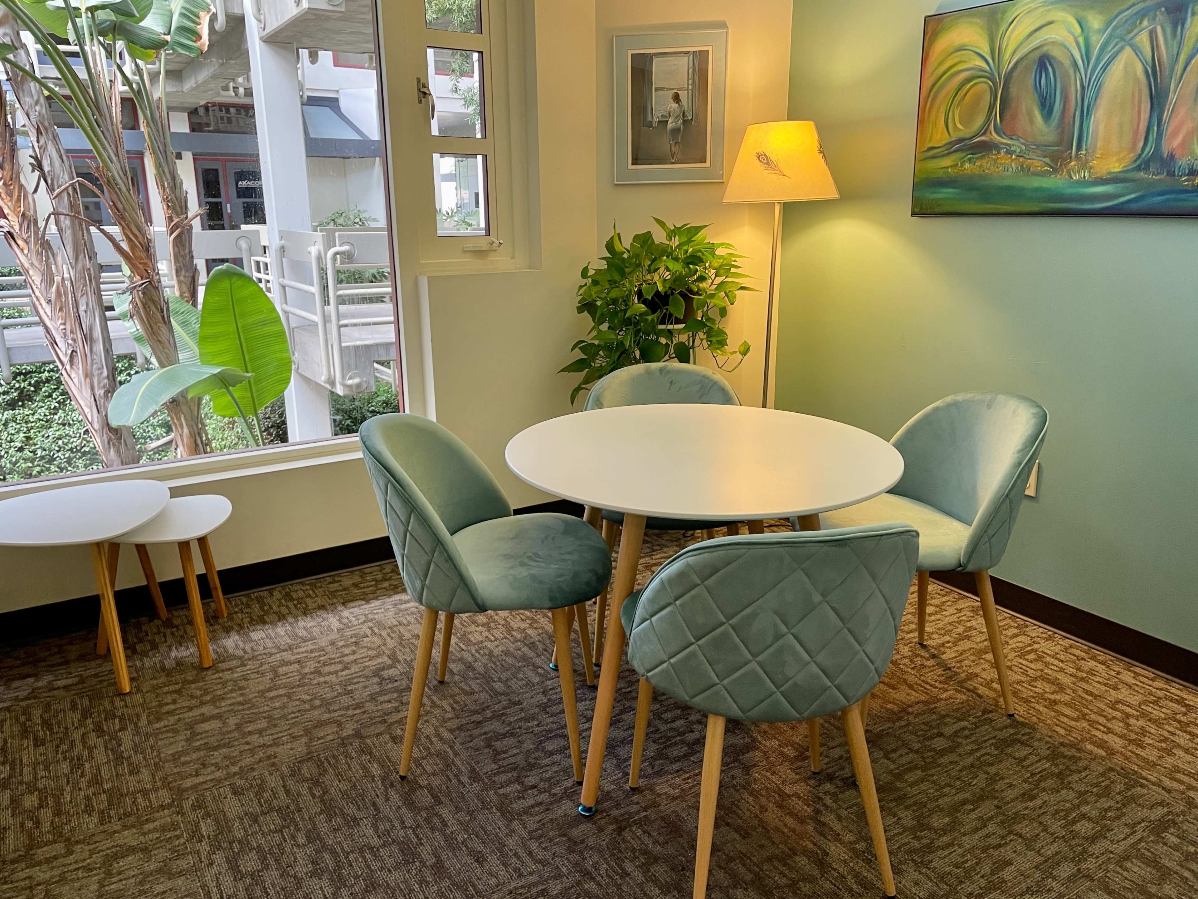 A small seating area features a round white table surrounded by four light blue chairs, with a lamp and a plant visible in the corner.
