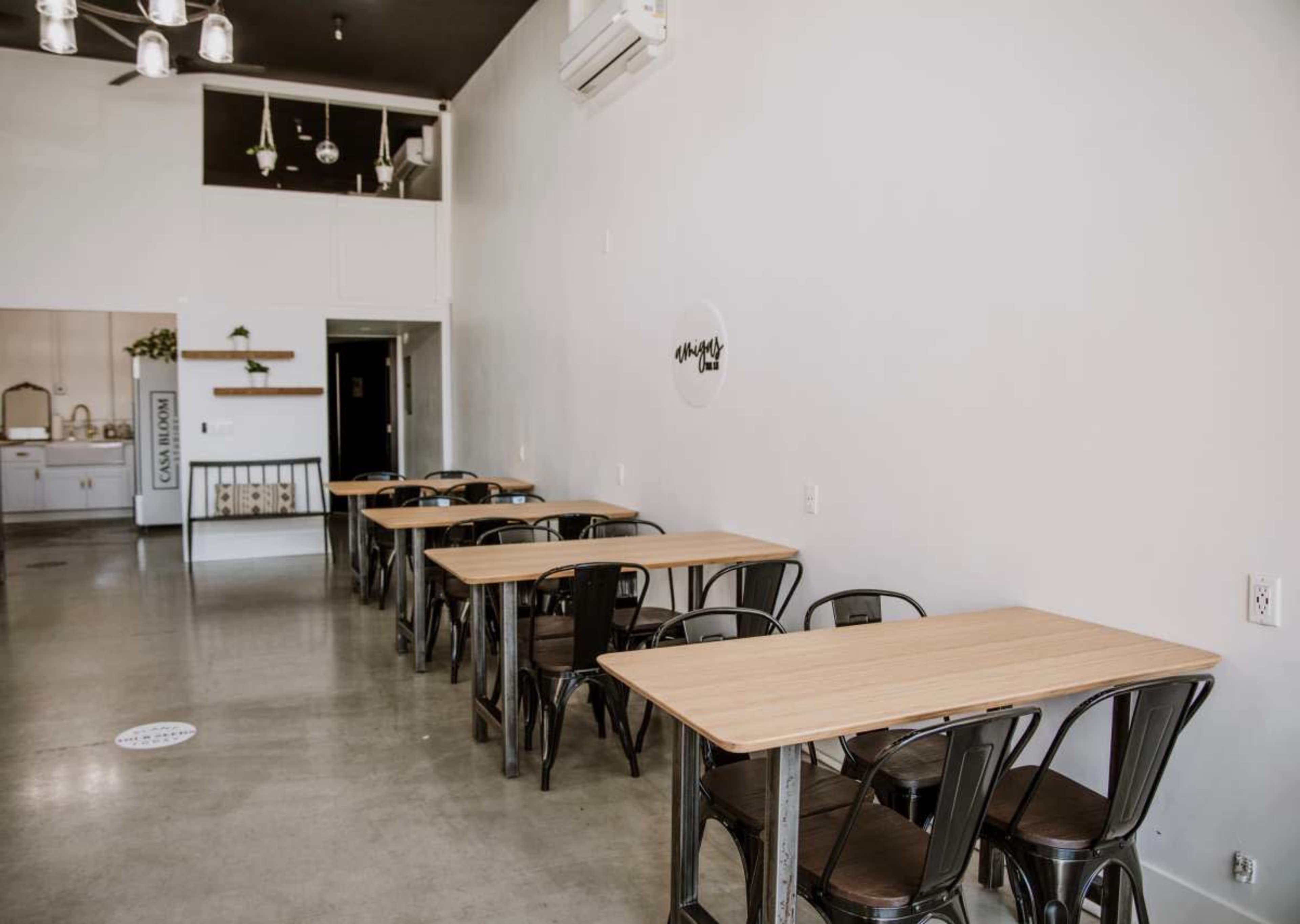 The image shows a minimalist café interior with several wooden tables and black metal chairs arranged in a spacious layout.