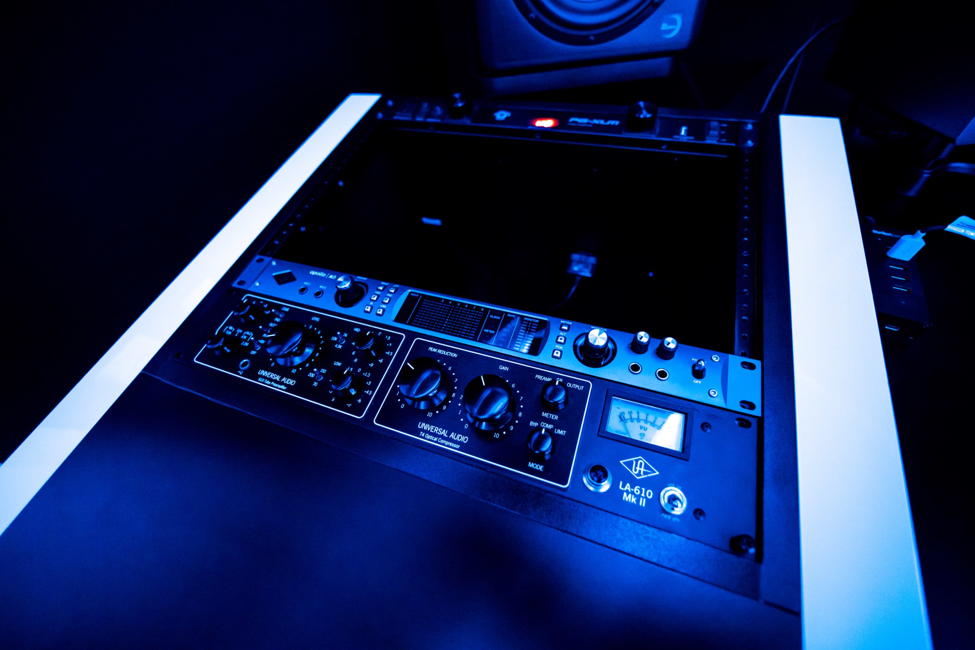 A power rack mount with various audio equipment, featuring knobs and displays in a blue-lit environment.