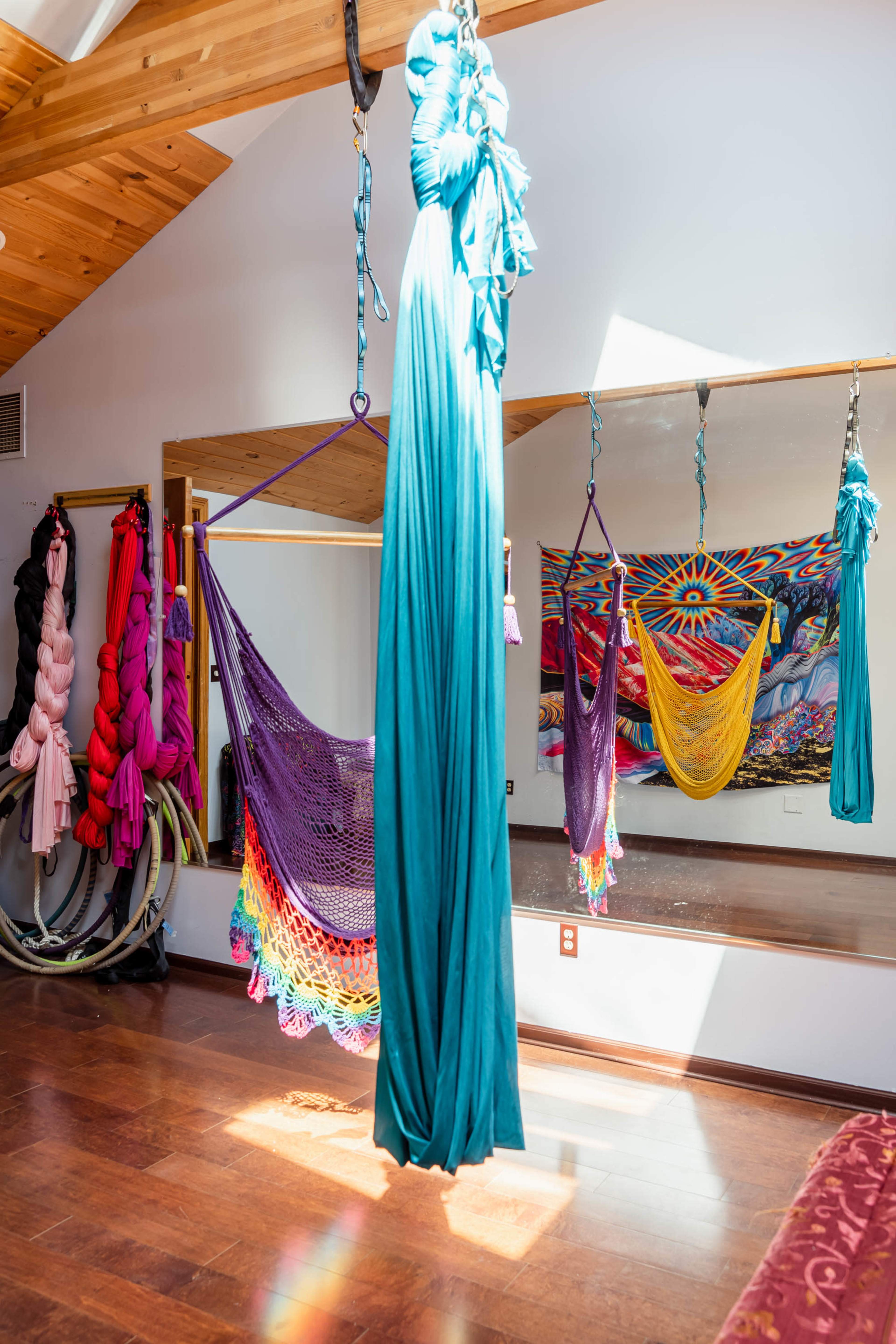 A brightly lit room with colorful aerial hammocks and fabric suspended from the ceiling, reflected in a large mirror.