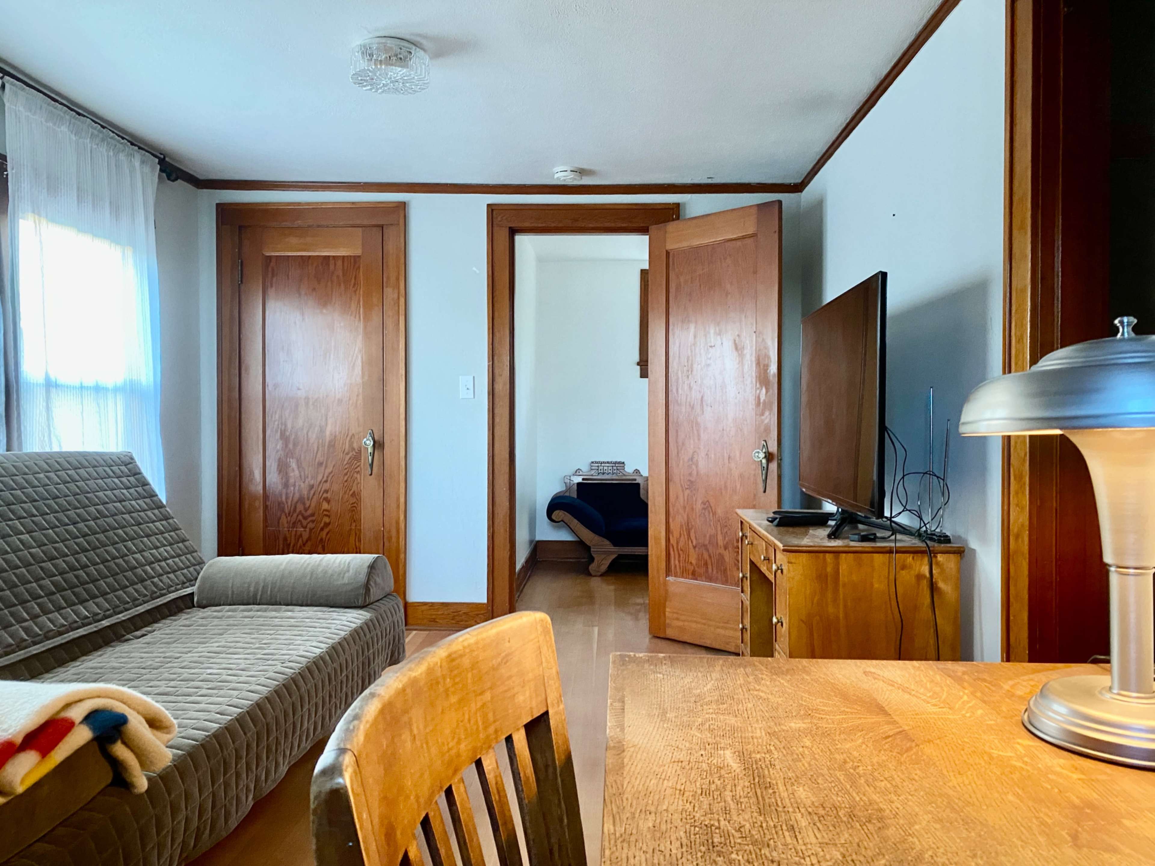The image shows a simple living room with a sofa, a wooden table, and open doors leading to another room.