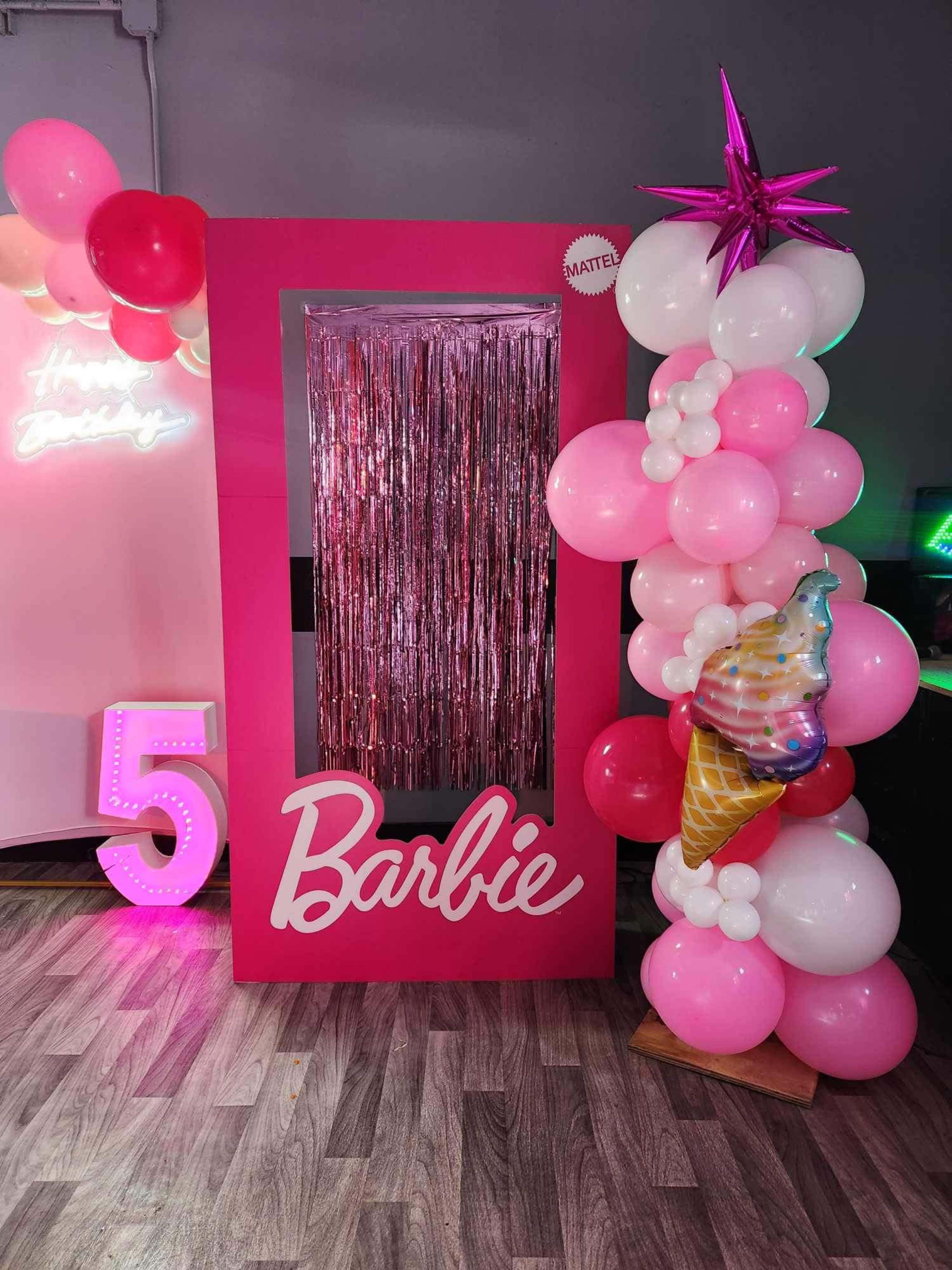 The image features a pink photo booth setup with a shiny curtain, labeled "Barbie," and adorned with pink and white balloons, along with a decorative ice cream cone.