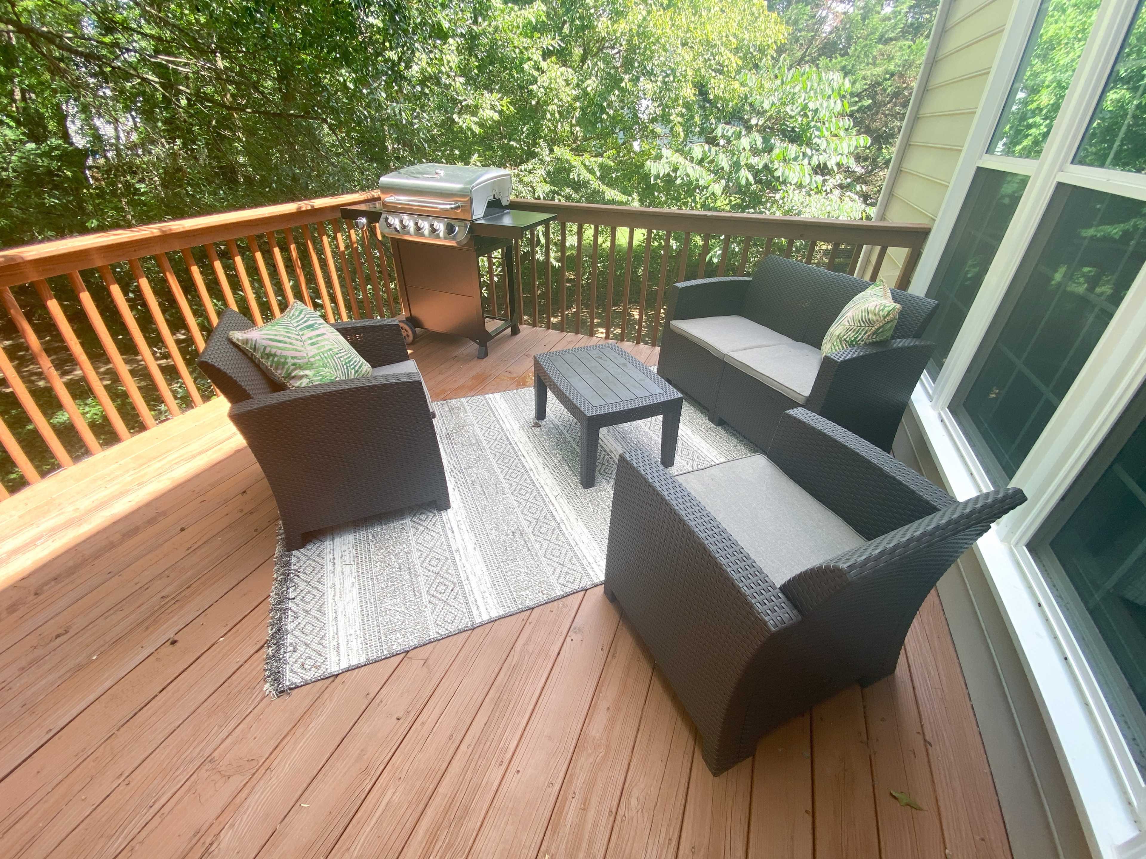 A deck features a seating area with two chairs, a loveseat, and a coffee table, along with a grill in the background.