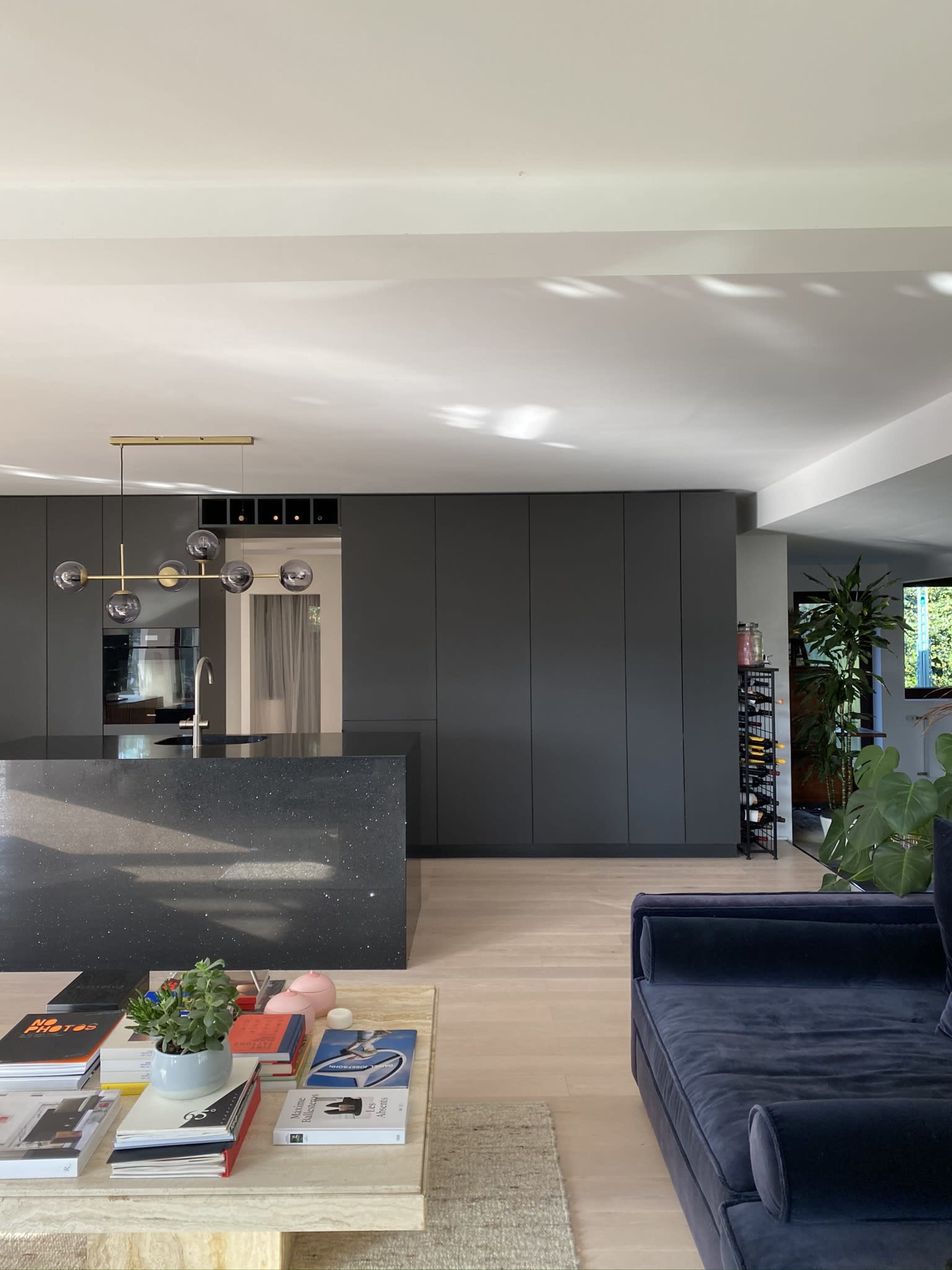 A modern kitchen with dark cabinetry, a black island, and a living area featuring a navy sofa and a coffee table with decorative items.
