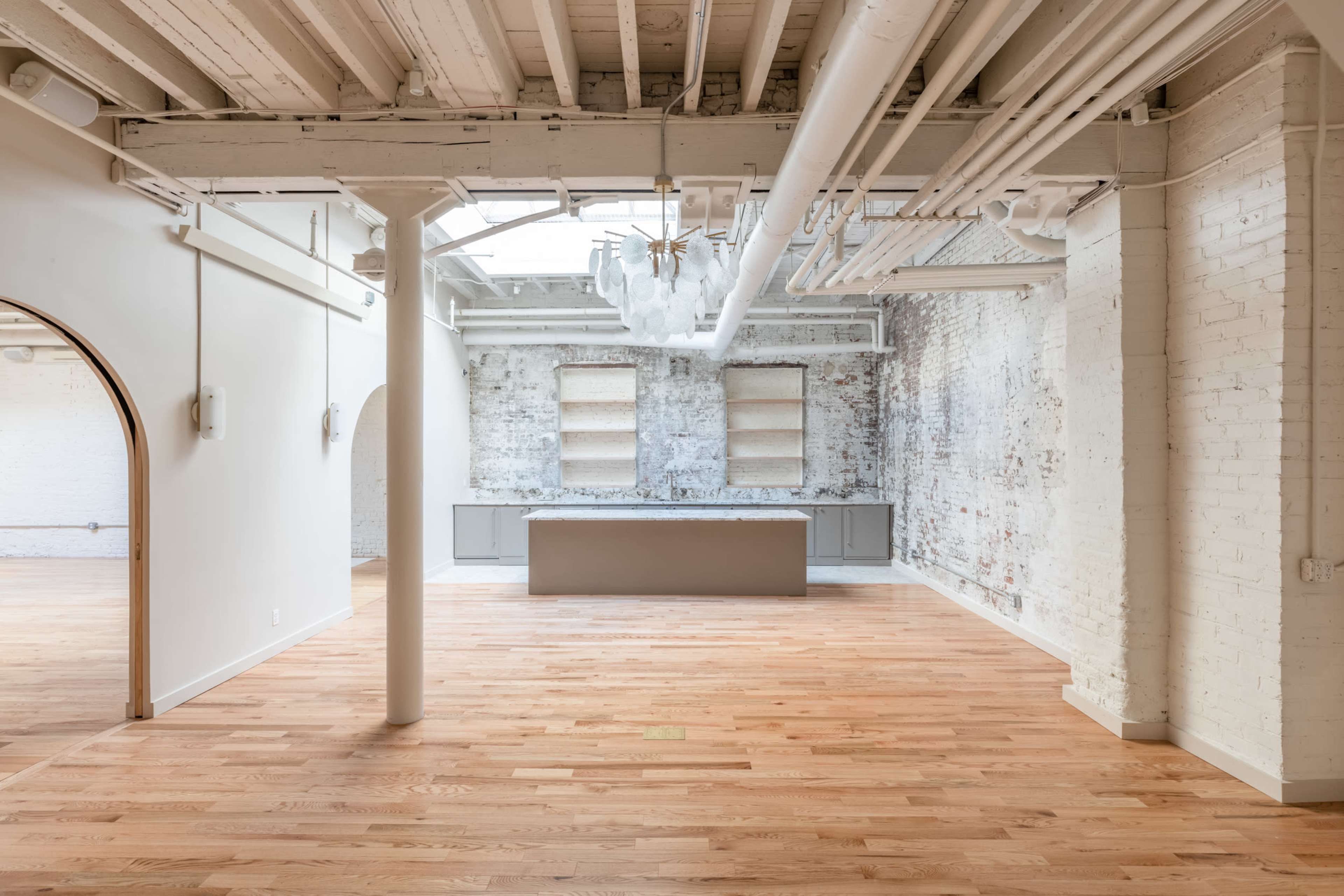 An open, spacious interior features hardwood floors, exposed brick walls, and a central island under a skylight.